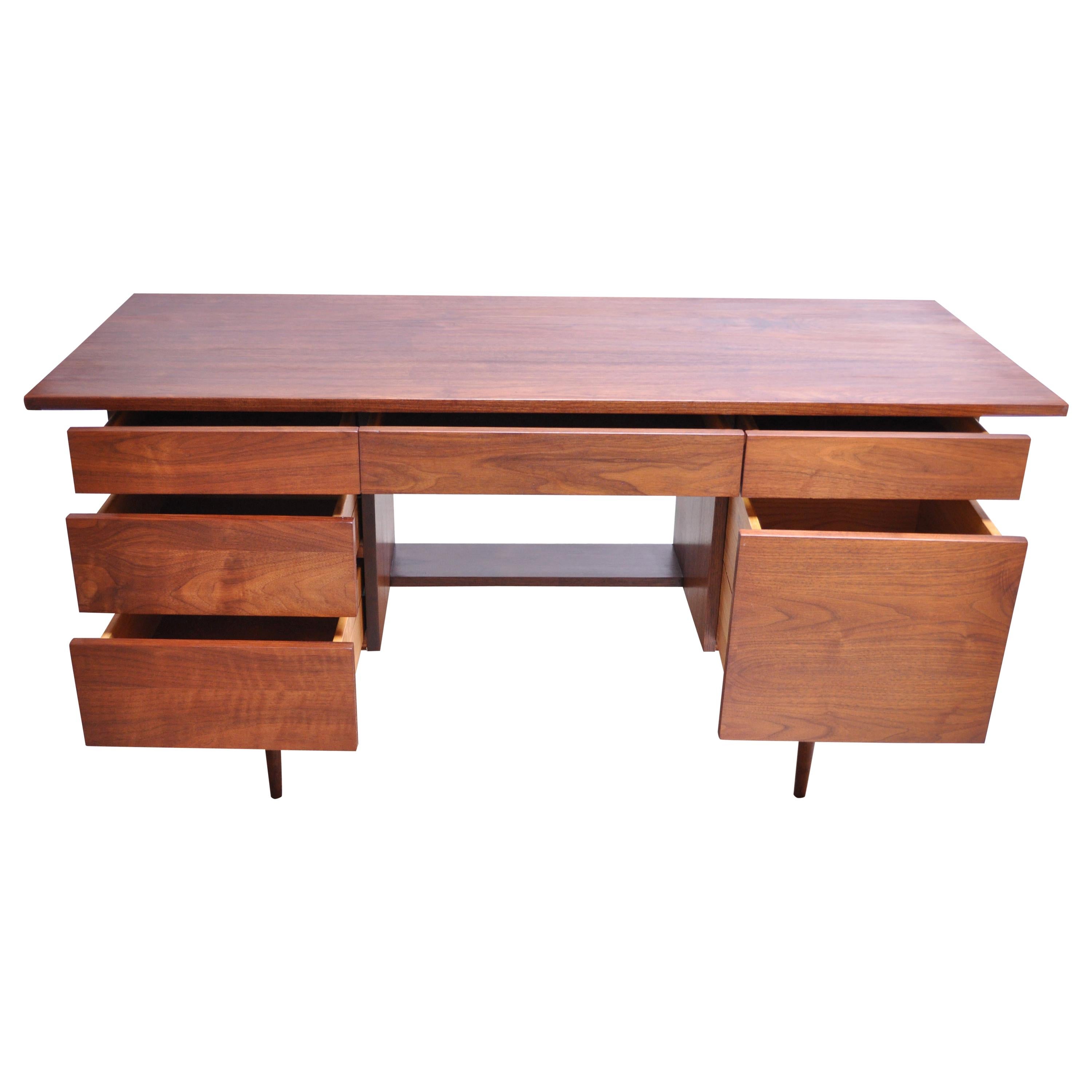 Minimal walnut student desk designed and manufactured by Mel Smilow in the 1950s. Offers ample storage with a row of three shallow drawers on top, one lower pull-out writing surface on the right side, and three larger lower drawers (two on the left