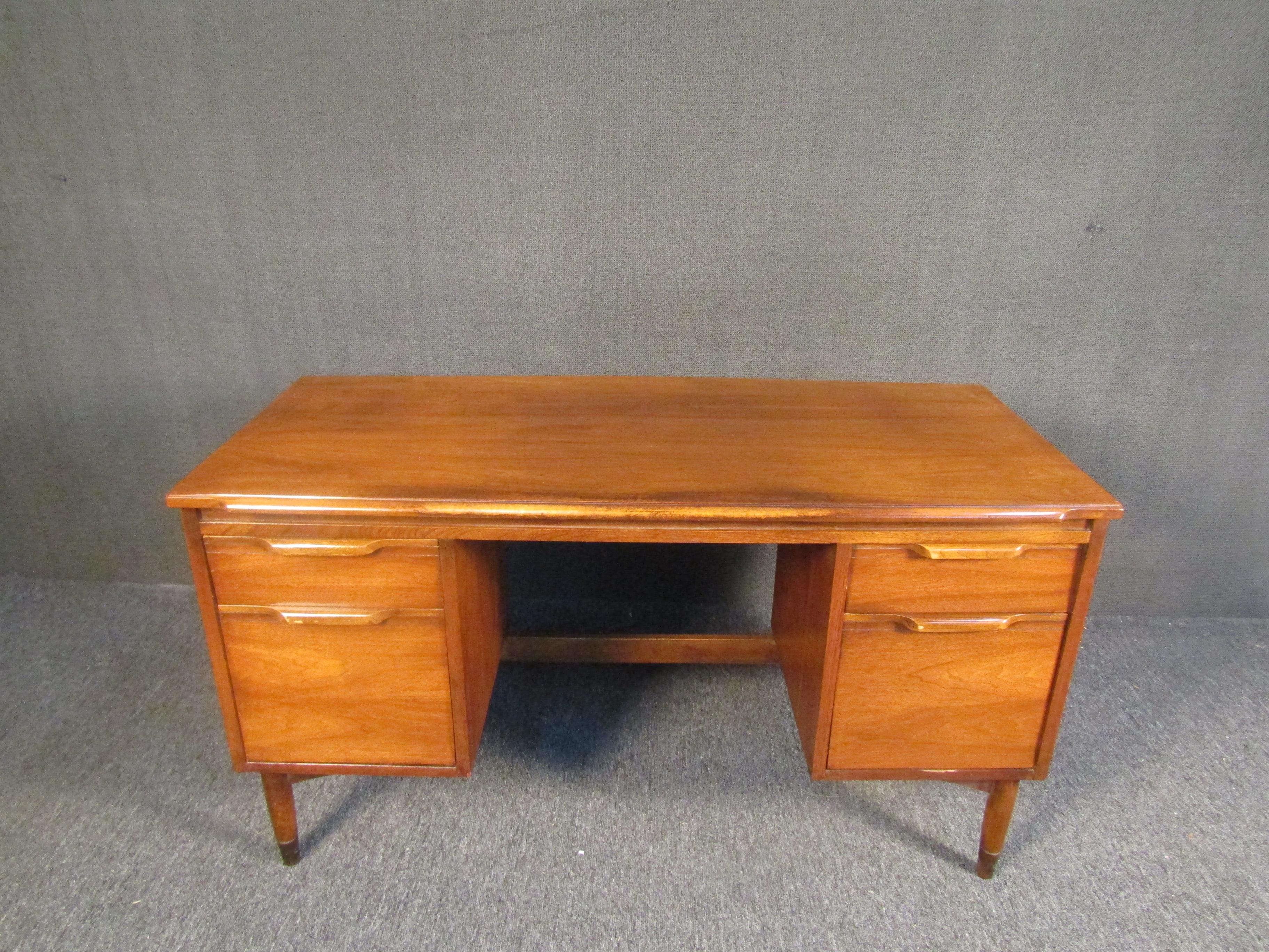 Vintage writing desk with a radiant walnut woodgrain and spacious drawers for filing papers or storing items. Sculpted legs and brass footing add an element of Mid-Century Modern style to this elegant and well-made desk. Please confirm item location