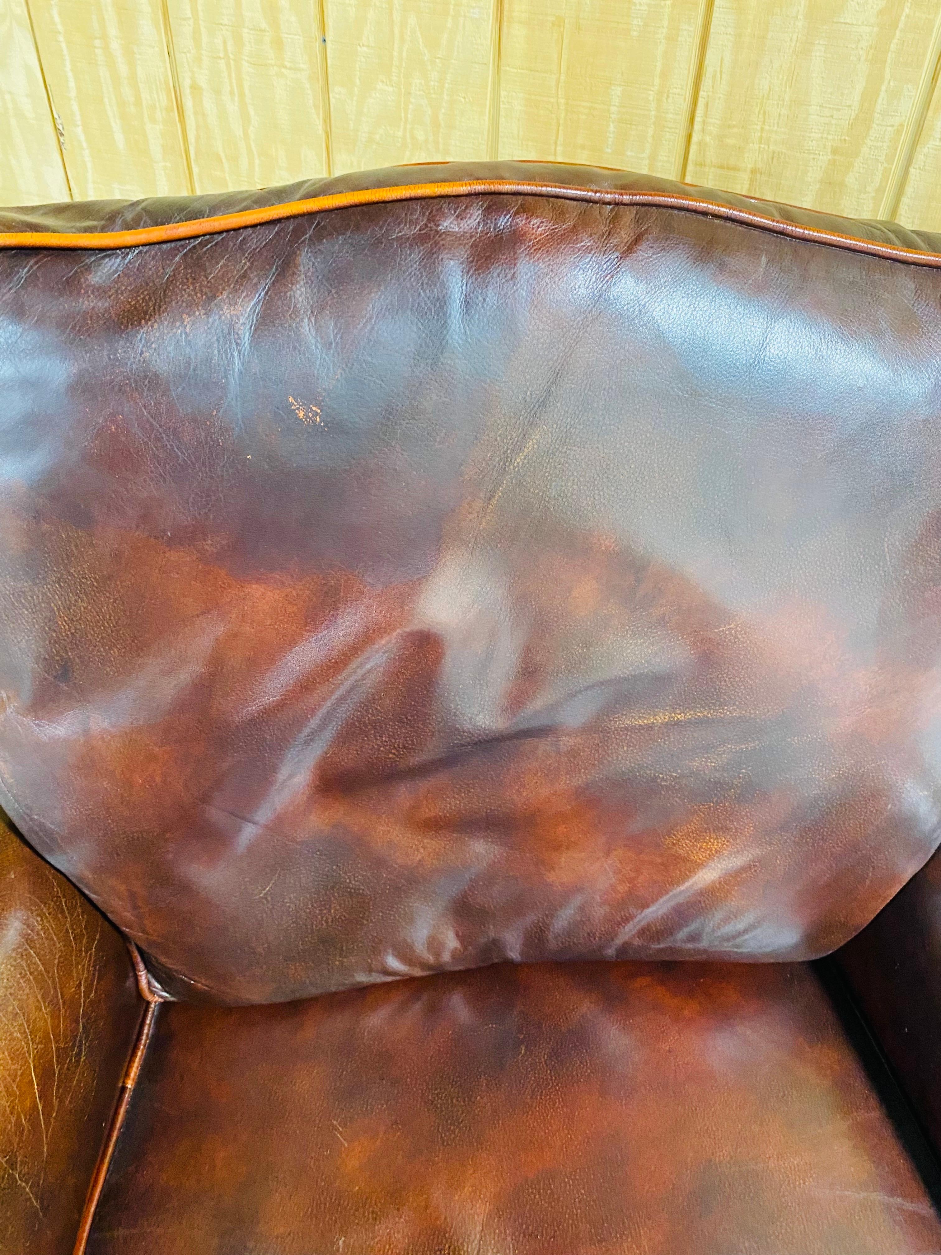 This is a vintage dark brown leather classical style club chair. This chair stands on a walnut Chippendale style frame and has dark brown weathered comfortable leather. The chair features solid brass hobnails on the edges and has the original North