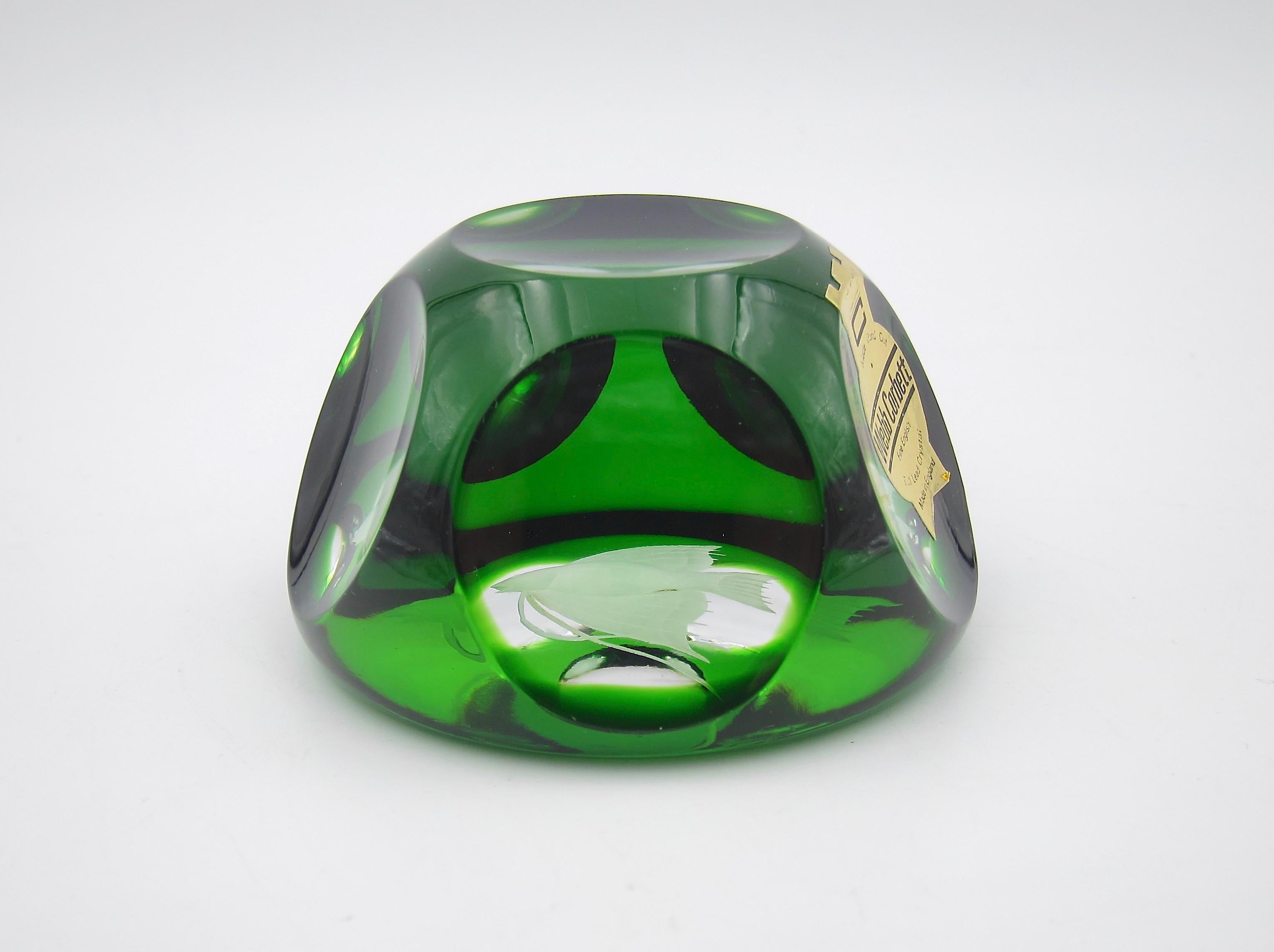 A vintage art glass paperweight from Webb Corbett (later Royal Doulton) of Great Britain, dating circa 1970s. The faceted weight is cased within a green layer of glass skillfully cut to clear. The faceting reveals an intaglio fish on the polished
