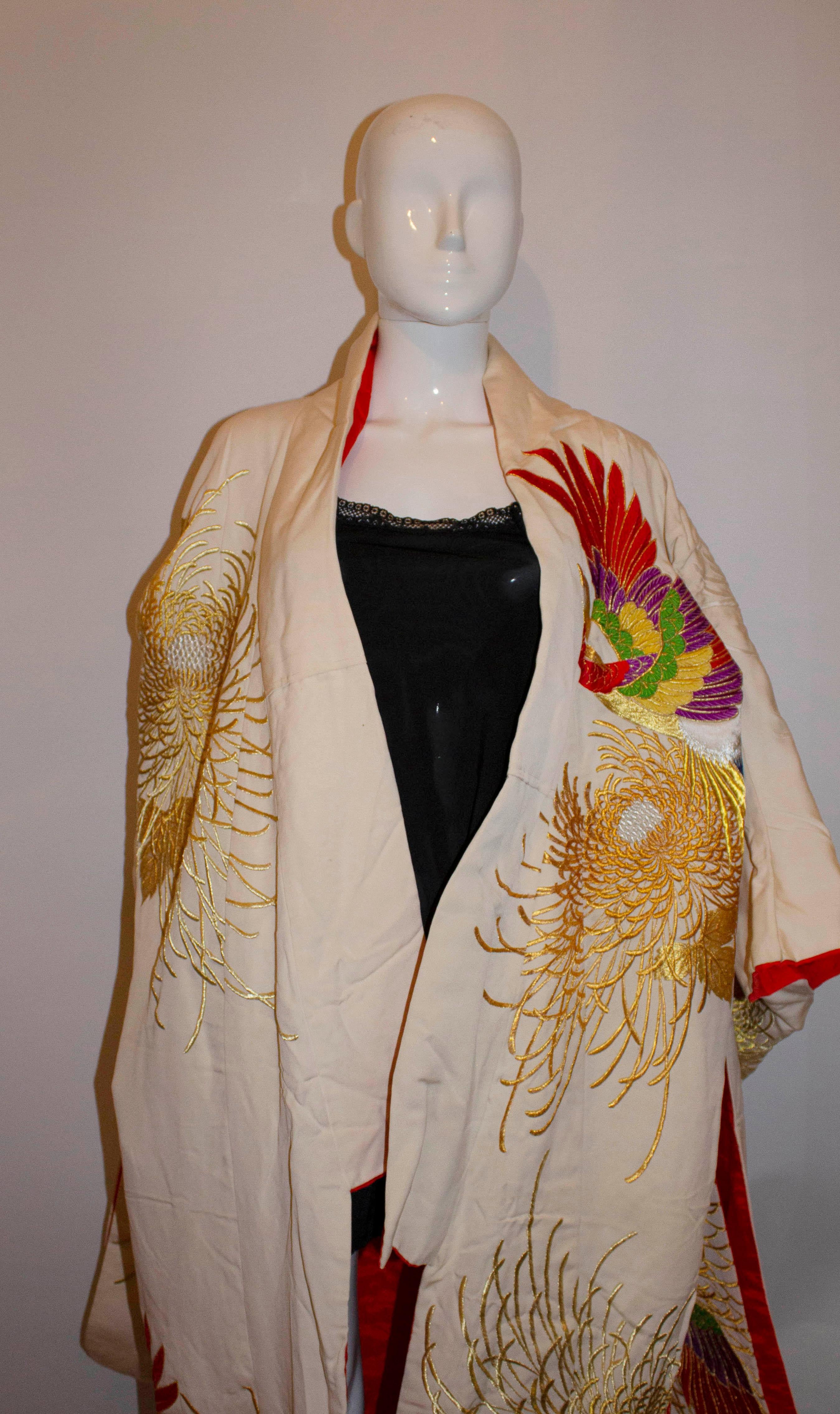 A vintage white silk kimono heavily embroidered with gold chrysanthemums and flying multicoloured phoenix. The phoenix fly through stylised gold and silver thread chrysanthemum flowers. The chrysanthemum flower or Kiku is the symbol of Japan and the