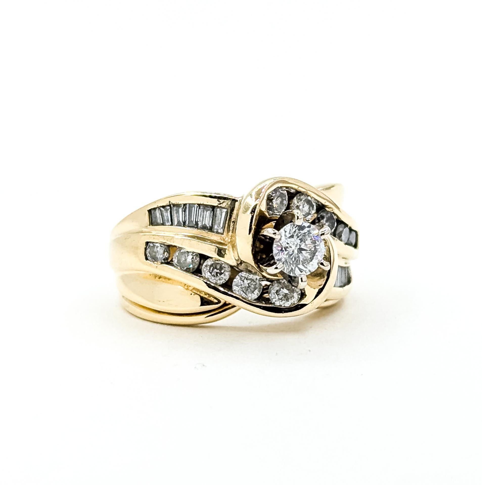 Dieser elegante Ring im Vintage-Stil ist aus 14 Karat Gelbgold gefertigt und zeigt in der Mitte einen runden Brillanten in Zackenfassung, der durch runde und Baguette-Diamanten in einem anmutigen, von Wellen inspirierten Design ergänzt wird. Das