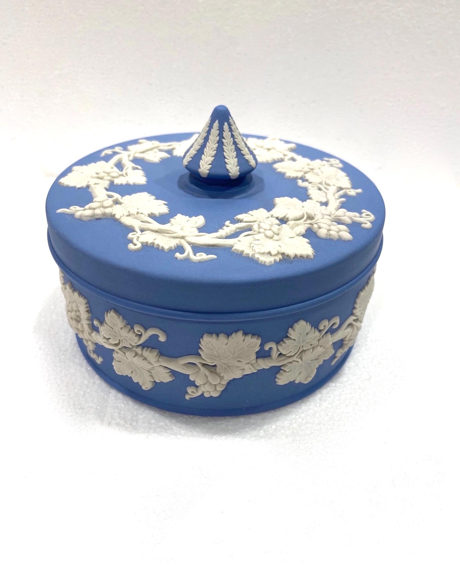 English porcelain box by Wedgwood from the jasperware pottery series. The lidded box features a matte biscuit or unglazed finish in blue with decorative relief work in contrasting white porcelain. The Neoclassical relief work has a foliage stem and