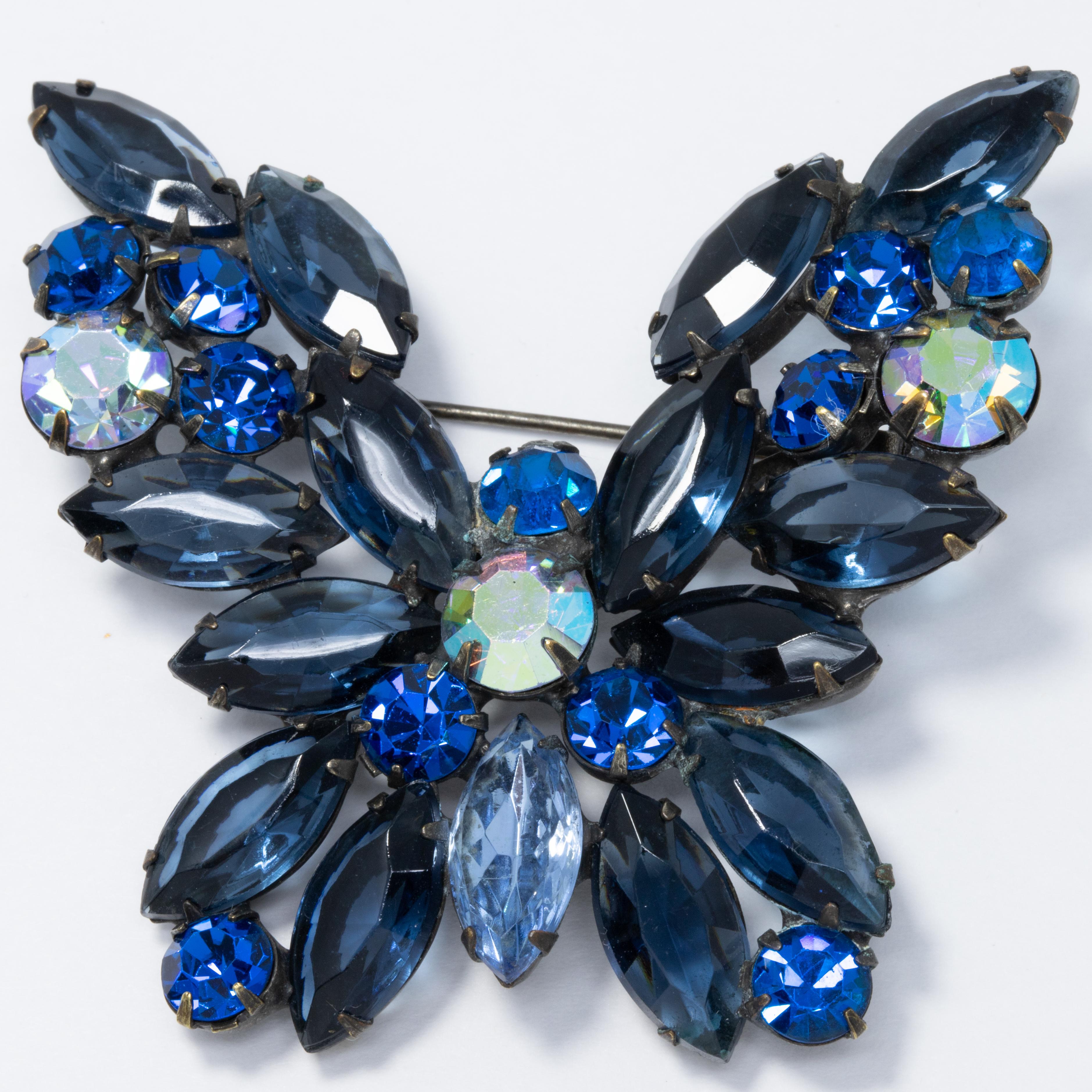 A sparkling butterfly pin brooch decorated with dazzling, prong set crystals. Features glittering sapphire, smoky blue, and aurora borealis colors colors on a gunmetal-tone setting.

Hallmarks: WEISS ©