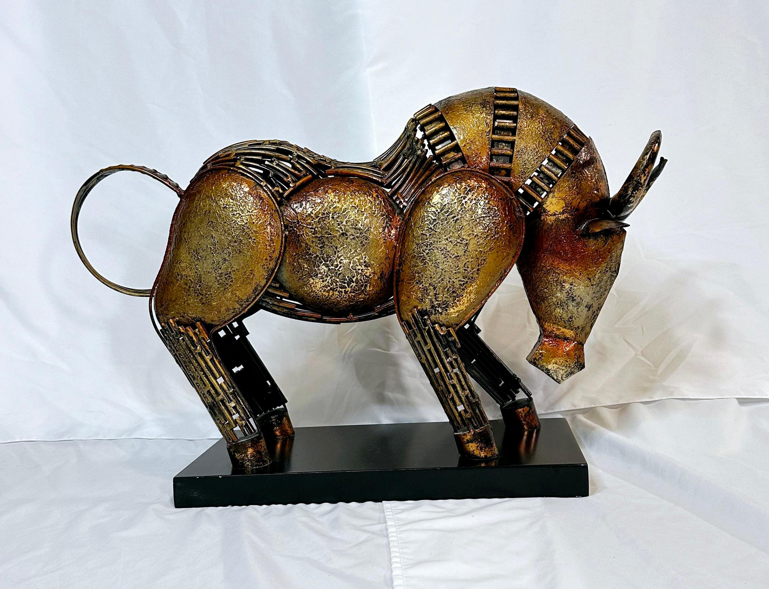 Brutalist style sculpture of a charging bull.
Heavy, solid piece. 
Statement piece. 
Perfect for a sofa or entry table.
Made of welded metal and painted with gold gradient.
Affixed to a black wooden base. 
Approximately 16 inches tall and 24 inches