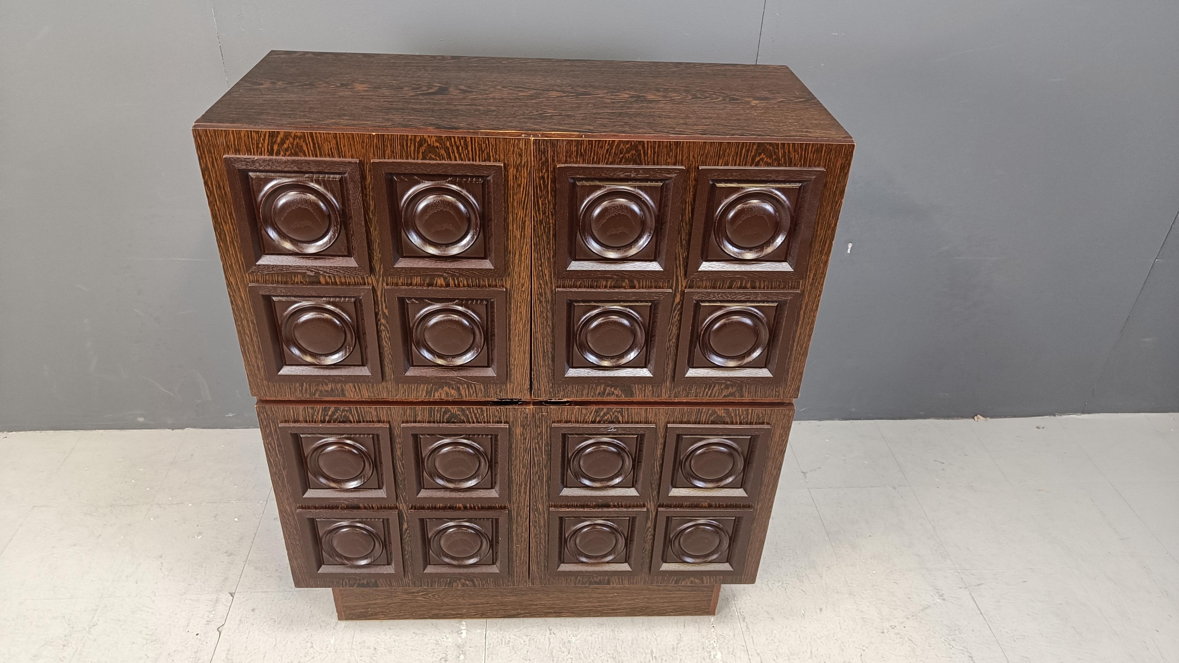 
Armoire à portes (bar) brutaliste en bois wengé graphique.

Meuble imposant offrant de nombreux espaces de rangement et réalisé en bois plaqué wengé (cadre et portes).

Bon état avec usure normale liée à l'âge.

Années 1970 - Belgique

Dimensions