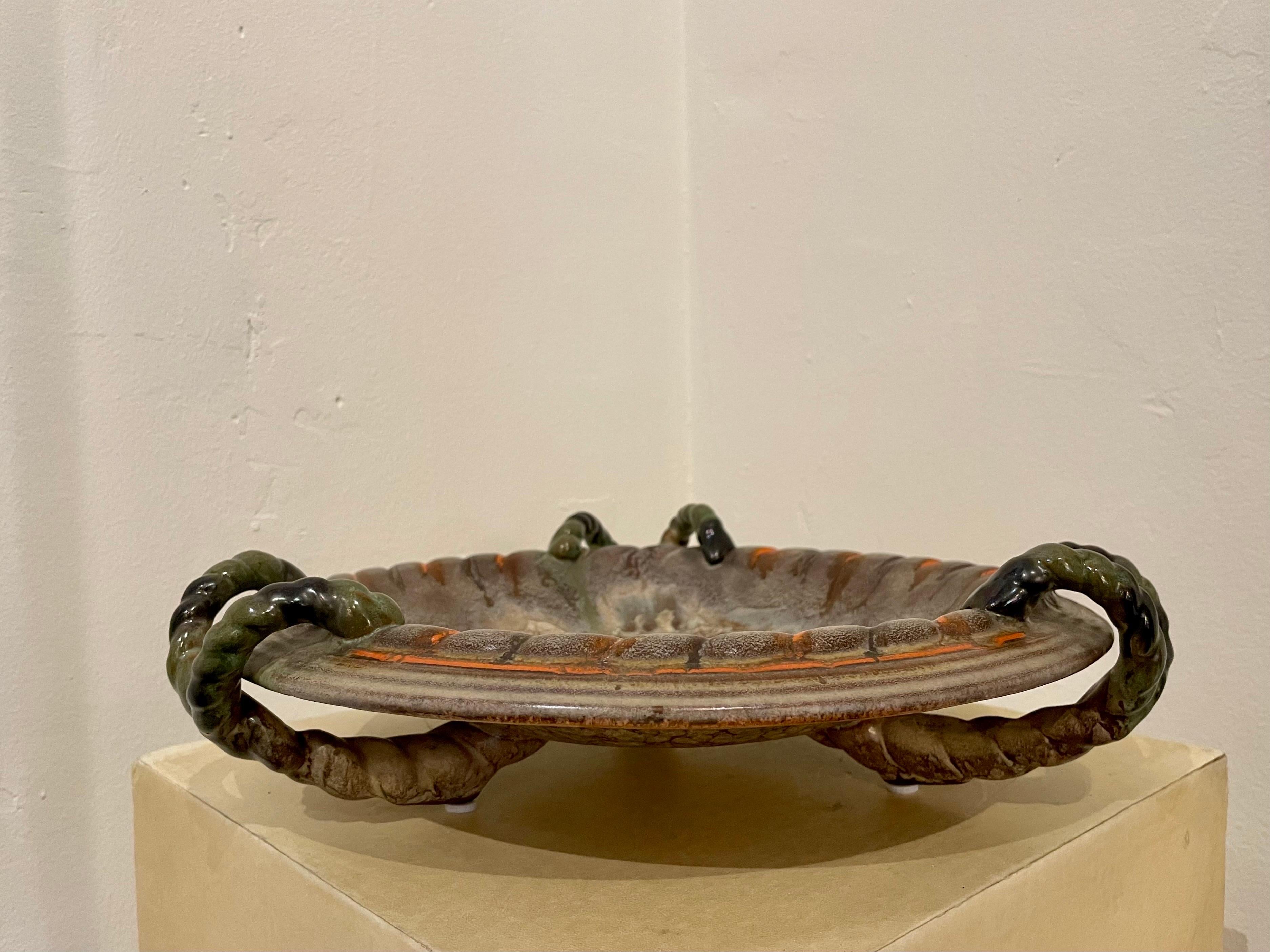 This ceramic bowl with three beautifully woven handles in green tones, highlight the richness of the orange and earth tone colors throughout the vessel. A very grand scale and perfect for any decor or table top. Stamped to bottom.