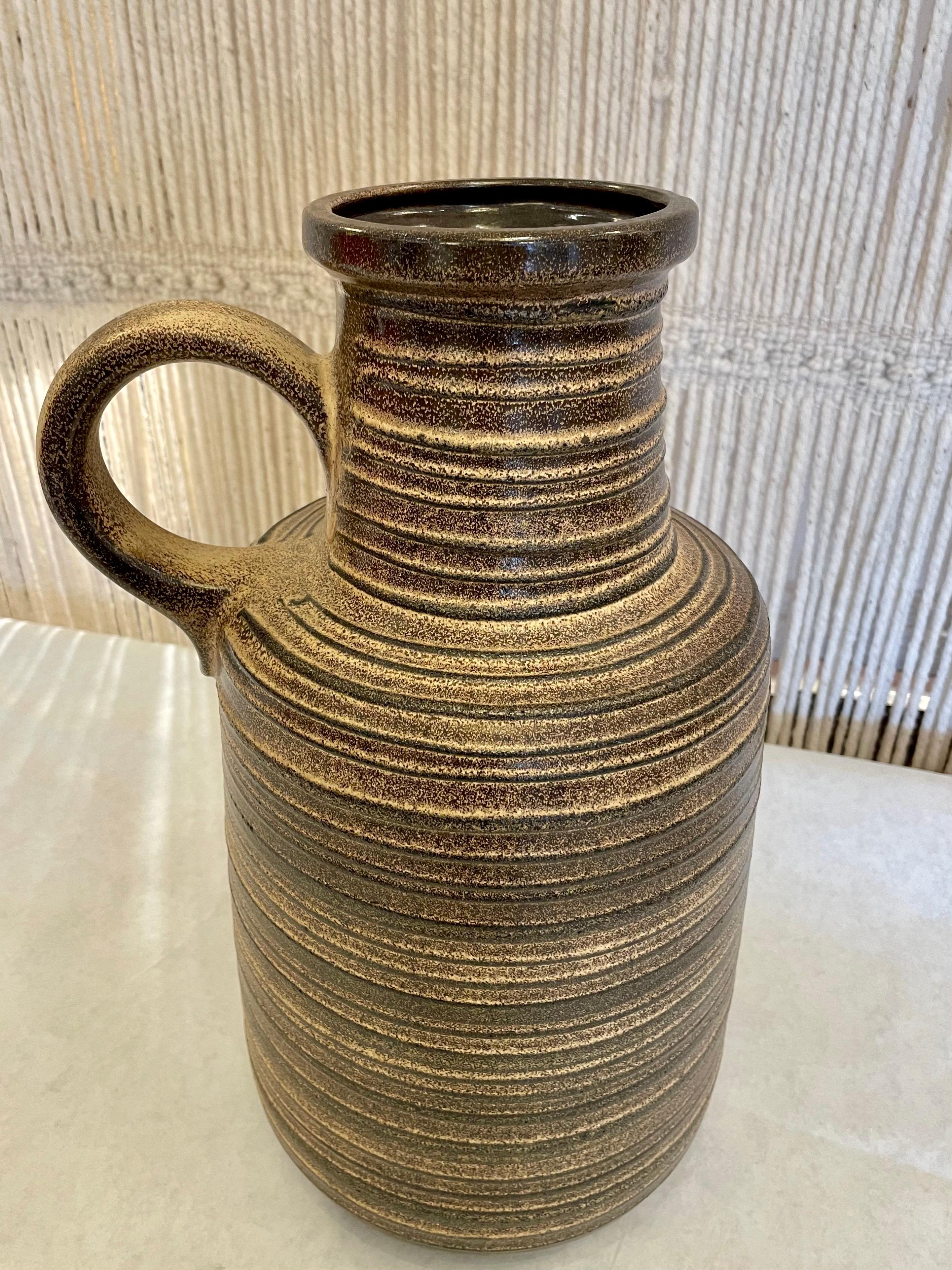 La texture côtelée de ce merveilleux vase en poterie ouest-allemande présente des tons bruns et beiges. Manche surdimensionné et en excellent état.