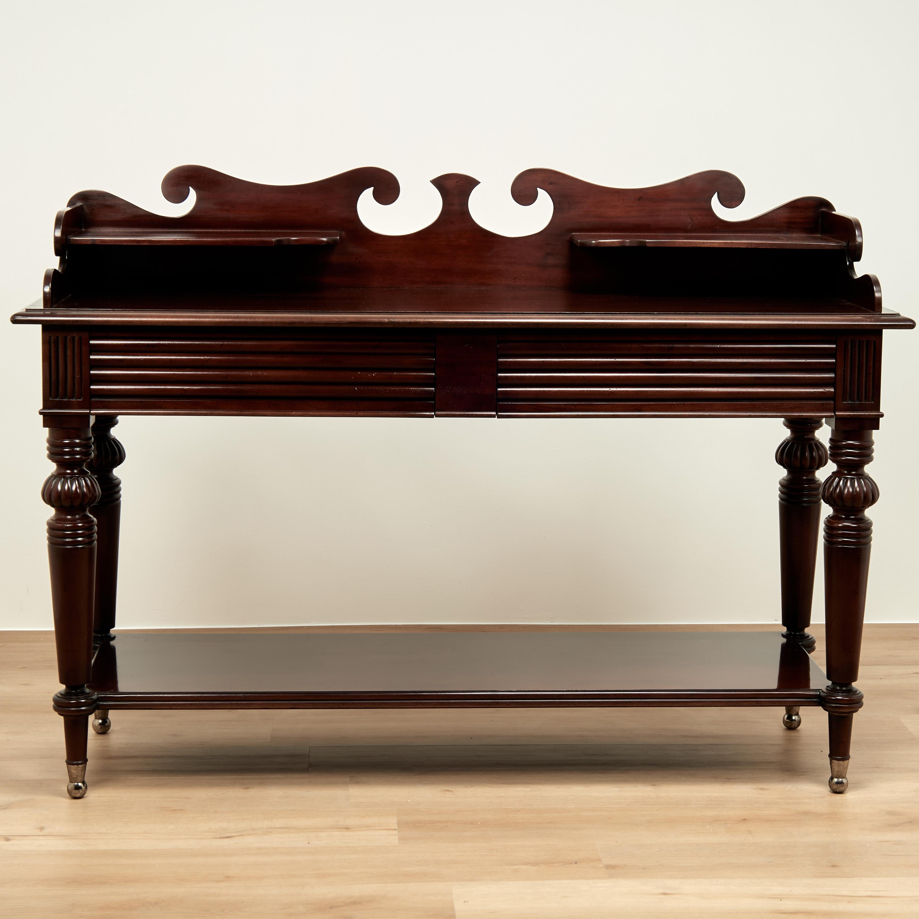 Handsome vintage British colonial style server crafted in mahogany in a West Indies style featuring a dramatic ocean inspired gallery with two shelves on a case with two beaded drawers set on turned and beaded tapered legs joined by a lower tire.