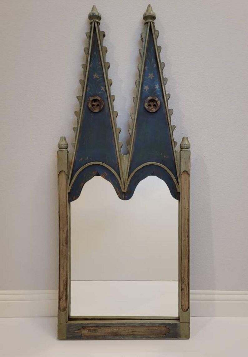 An imaginative hand painted architectural castle style mirror. 

Featuring a vertical rectangular mirror in a fanciful sculptural wooden frame with two tall steeple like finial topped points that give the impression of a Medieval castle.