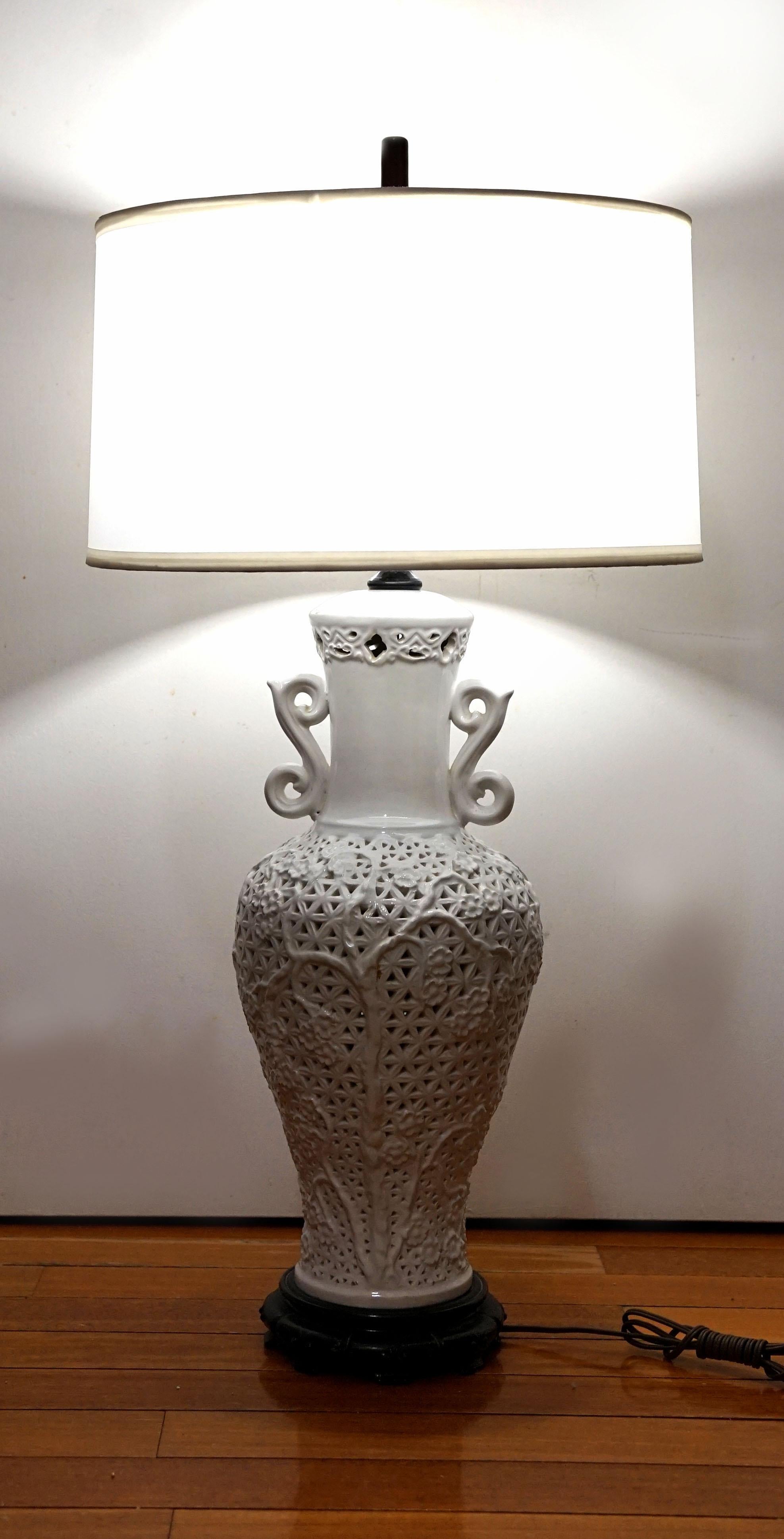 This is a Chinese Blanc de Chine White Porcelain vase form lamp, dating back to the period between 1960-1990.. The silhouette in pierced white porcelain--blanc de chine--the scroll ears, and the silk white barrel lamp shade make this an elegant