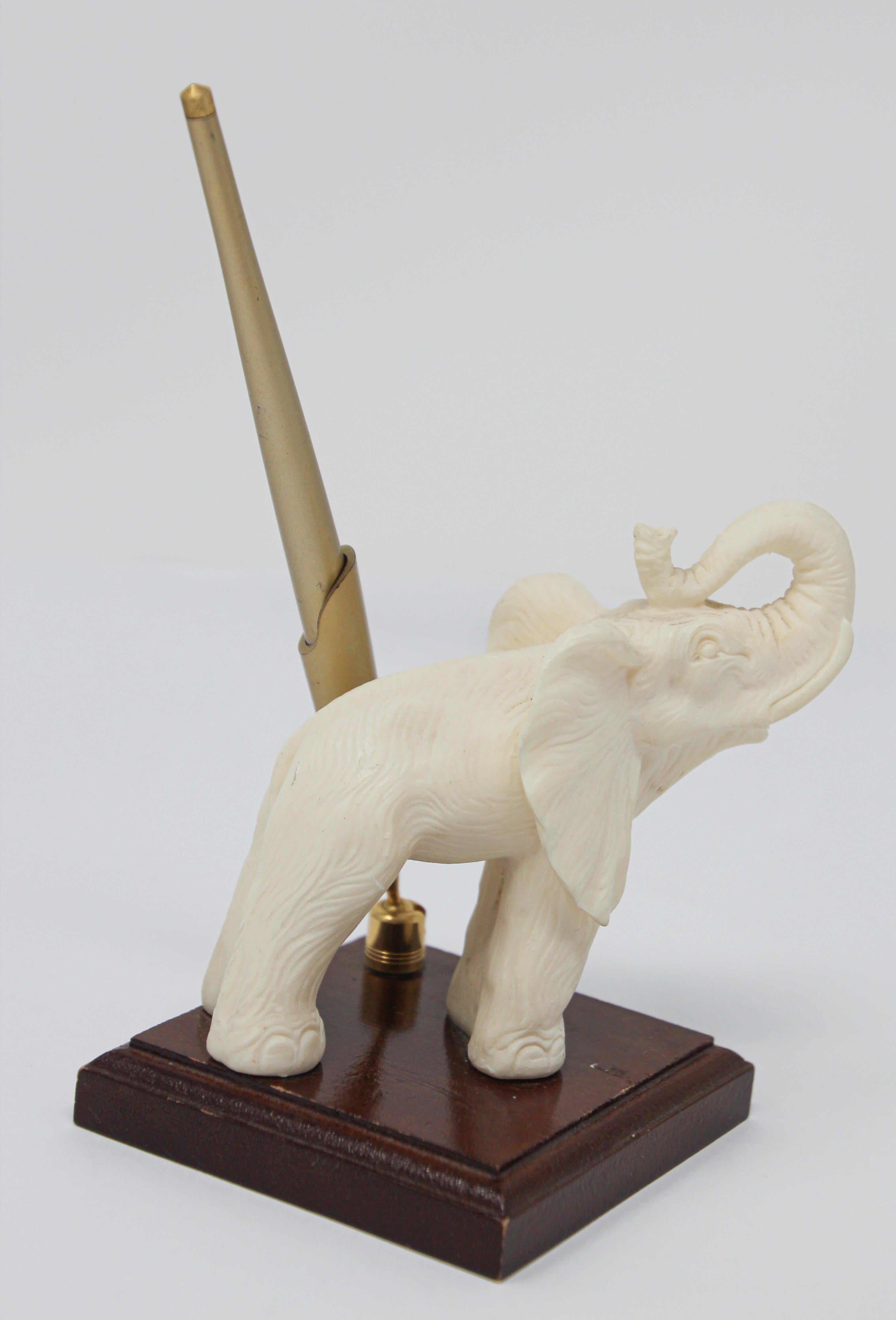 Elegant cast composite vintage sculpture that show a white elephant with his trunk up presented on a wooden stand and next to it a brass pen.
The representation of elephant in Asia represent wisdom, longevity and white is for peace.
White elephant