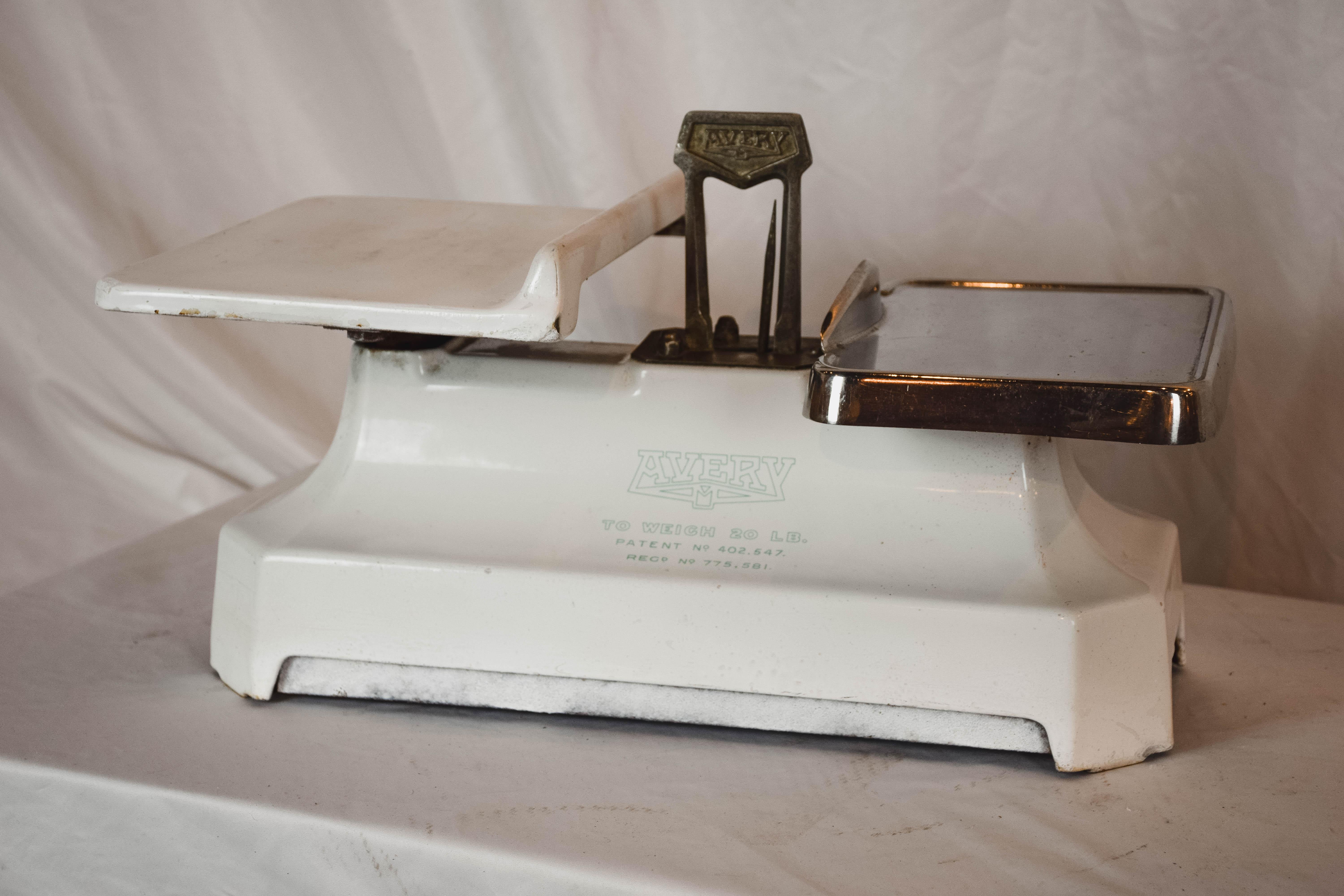 Charming 1950s white enameled Avery shop balance scale. This scale with the Avery emblem on its enameled base and one porcelain tray and one stainless steel has great vintage appeal, and would look great in a kitchen, a restaurant or shop.