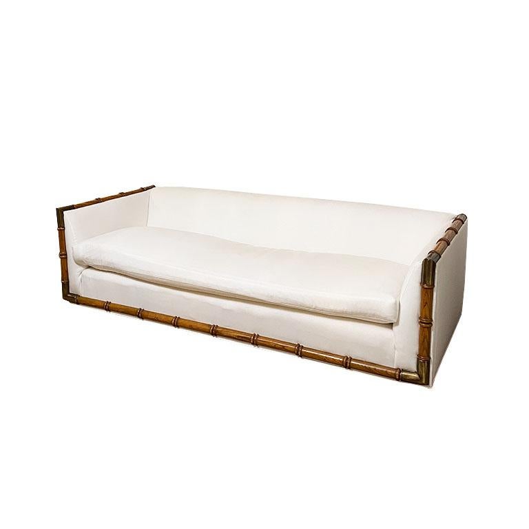A long vintage Ethan Allen sofa reupholstered in a crisp milky white. Faux bamboo accents frame the couch around the bottom and sides, with brass on each corner. 

The bench cushion in the middle has been reimagined from its original three seat