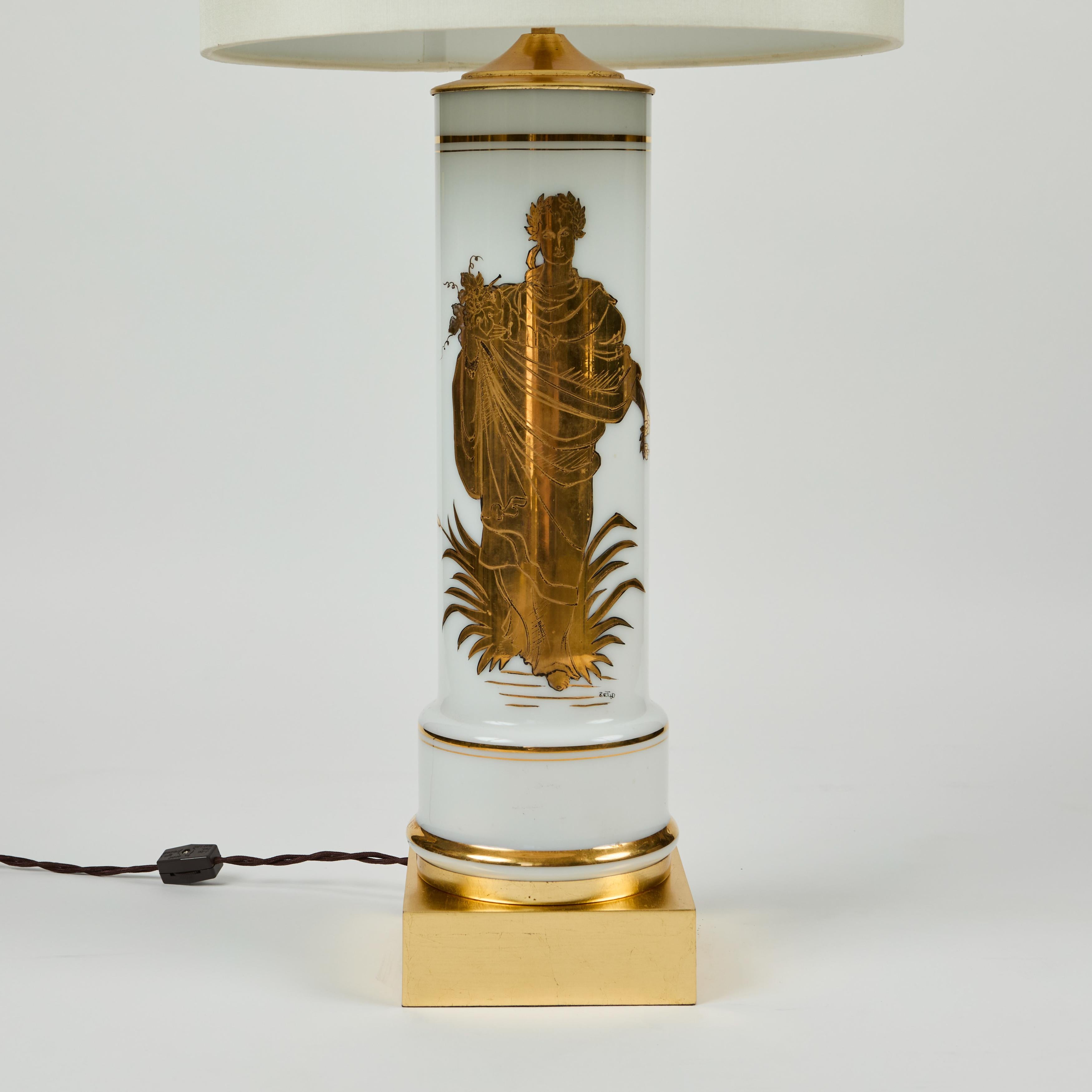 This vintage white glass cylinder based lamp is decorated with a descriptive and illuminating gold Greek figure holding an abundant cornucopia. The base and cap have been newly gold leafed and the lamp newly rewired. This piece has been paired with