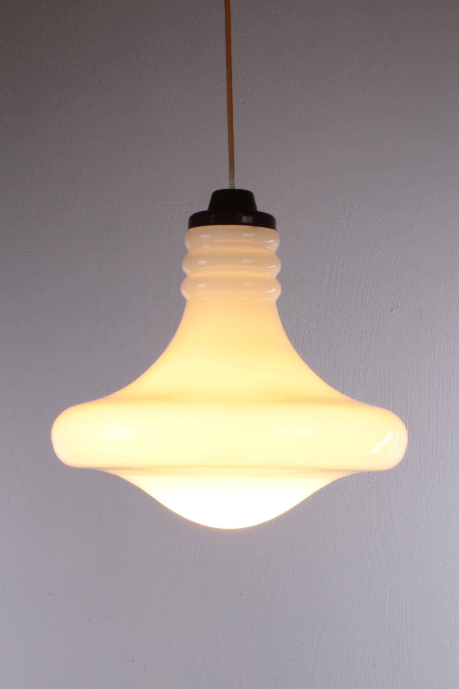 This is a beautiful white glass pendant lamp, whose designer is unfortunately unknown to us.

The lamp is made of white glass with a brown plastic cap. The lamp was produced in Germany around the 1960s.

At the top are beautiful blown rings and