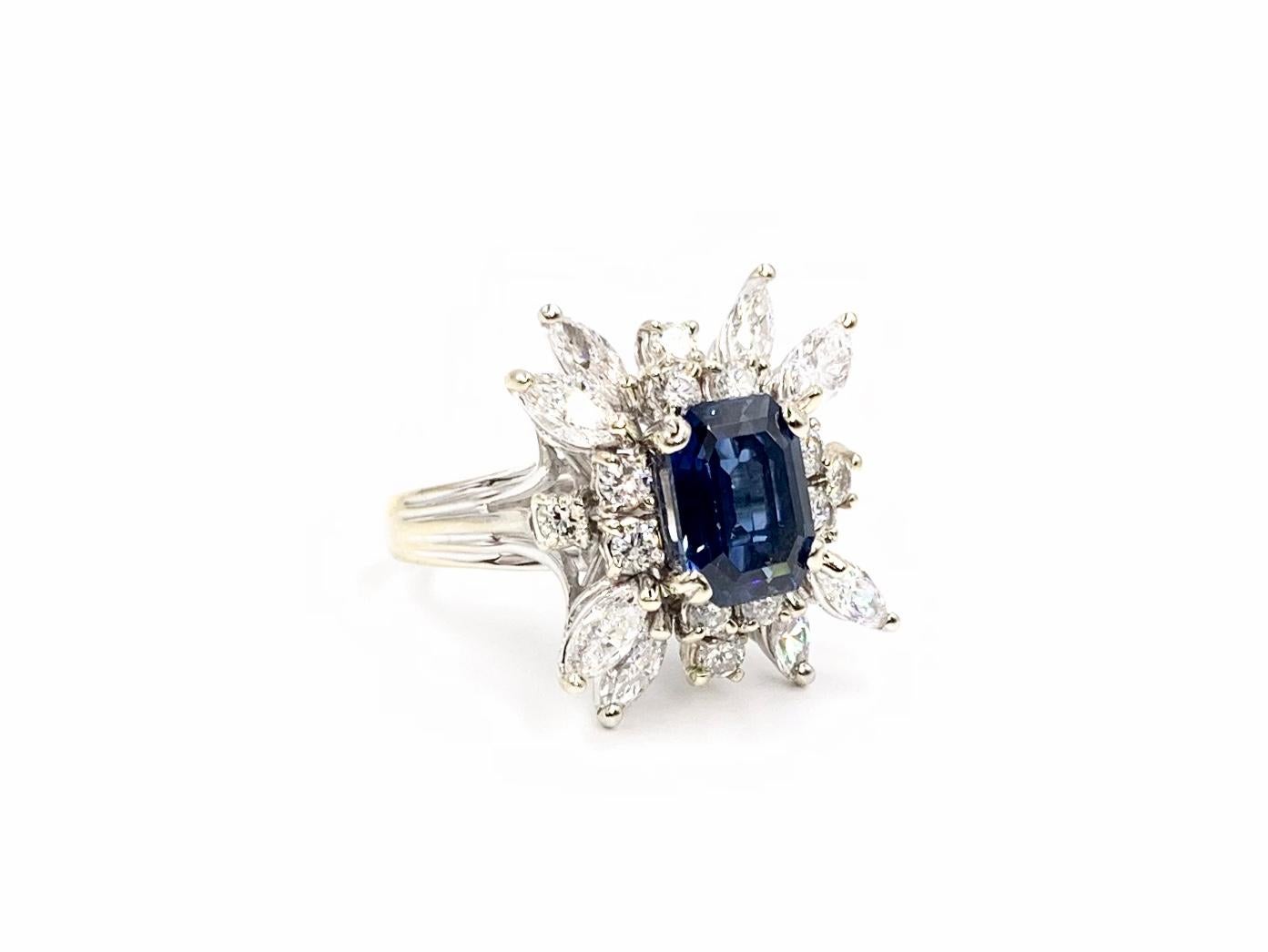 Circa 1975, this beautiful 14 karat white gold cocktail ring features a well saturated and vivid 2.80 carat emerald cut blue sapphire with medium transparency surrounded by approximately 1.60 carats of round brilliant and marquise cut white diamonds