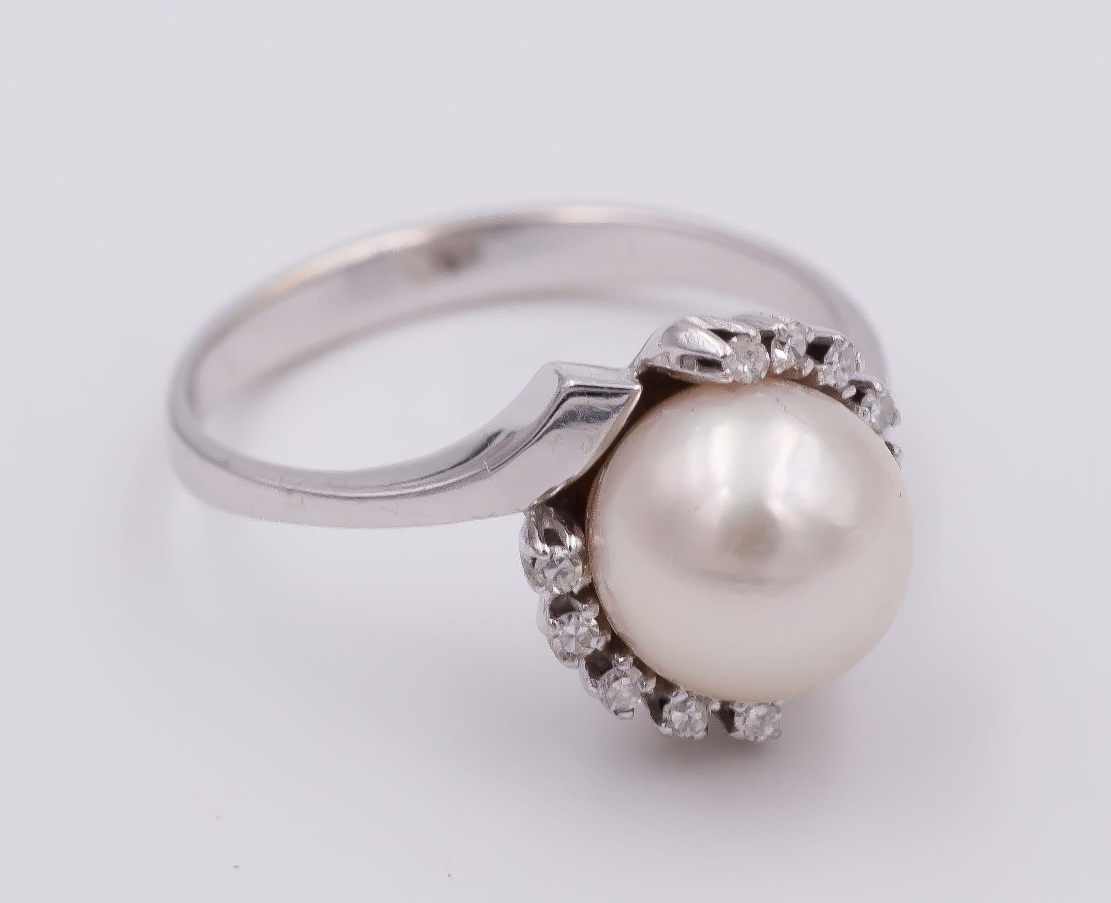 A simple but refined vintage ring: it is crafted in white gold throughout and it is set with a central pearl, surrounded by ten round cut diamonds. 
The shoulders of the ring are divided in two, giving to the jewel a nice and interesting movement.