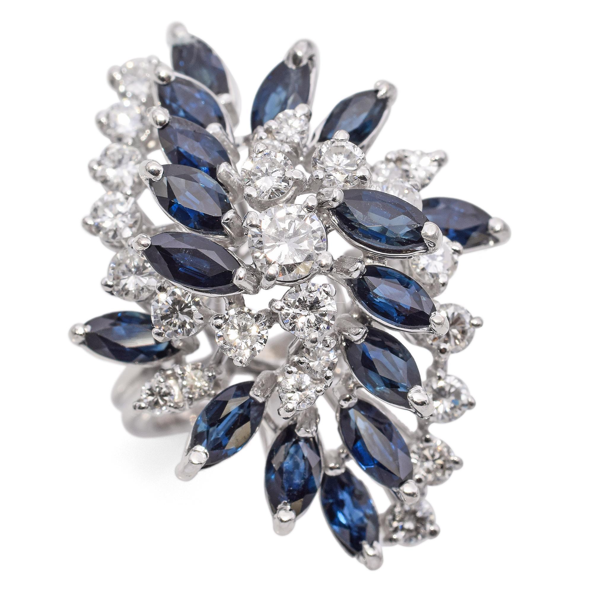 Elegant Statement Cluster Ring in White Gold. This striking ring features a stunning array of marquise-cut blue sapphires, totaling 2.88 carats, beautifully complemented by round-cut white diamonds weighing 1.45 carats.

Weight: 12.2