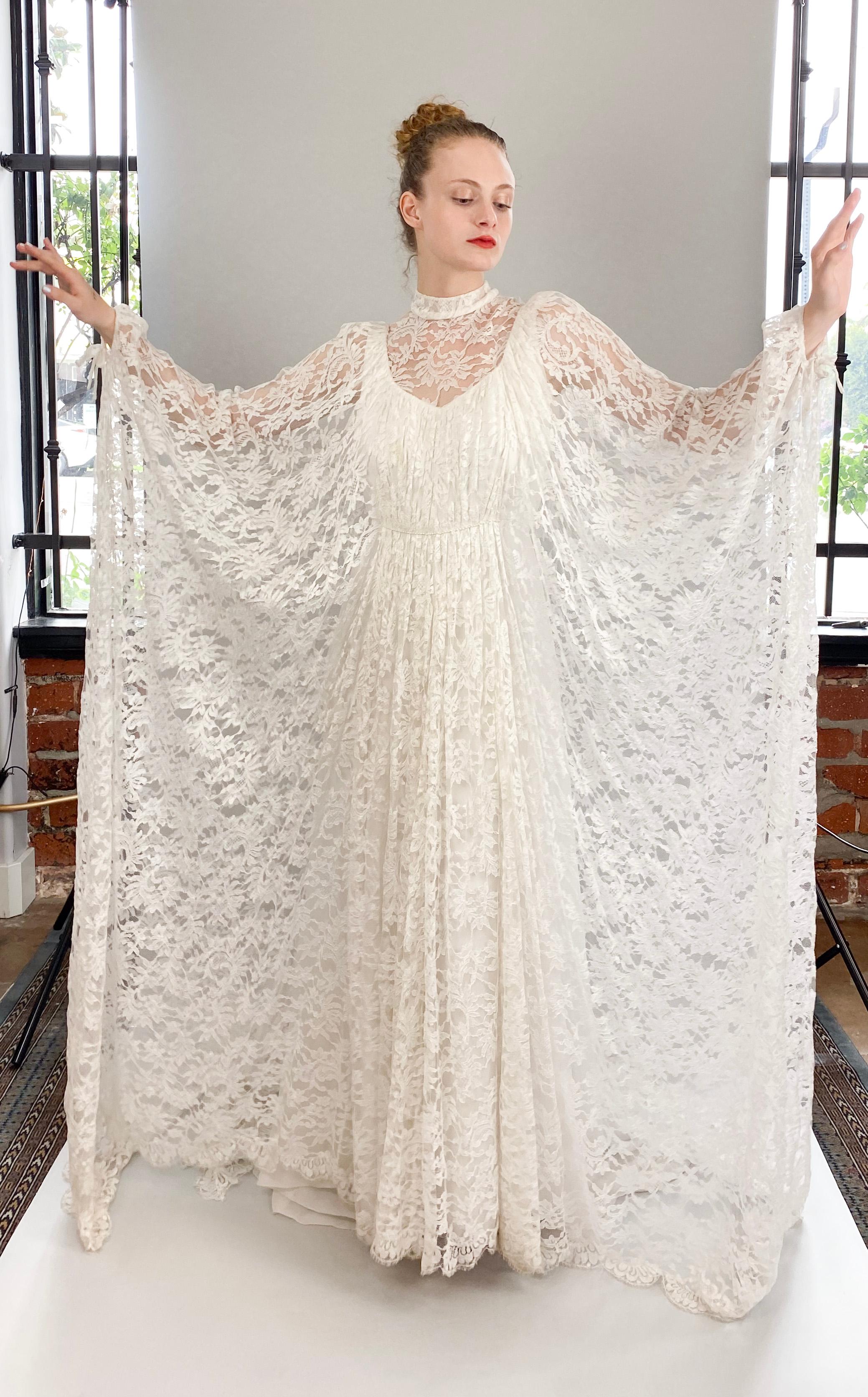 Cette superbe robe de mariée vintage en dentelle blanche présente d'élégantes manches chauve-souris et une traîne délicate. Avec ses perles à la taille et son col montant, elle respire la sophistication et la grâce. Les liens sur les manches