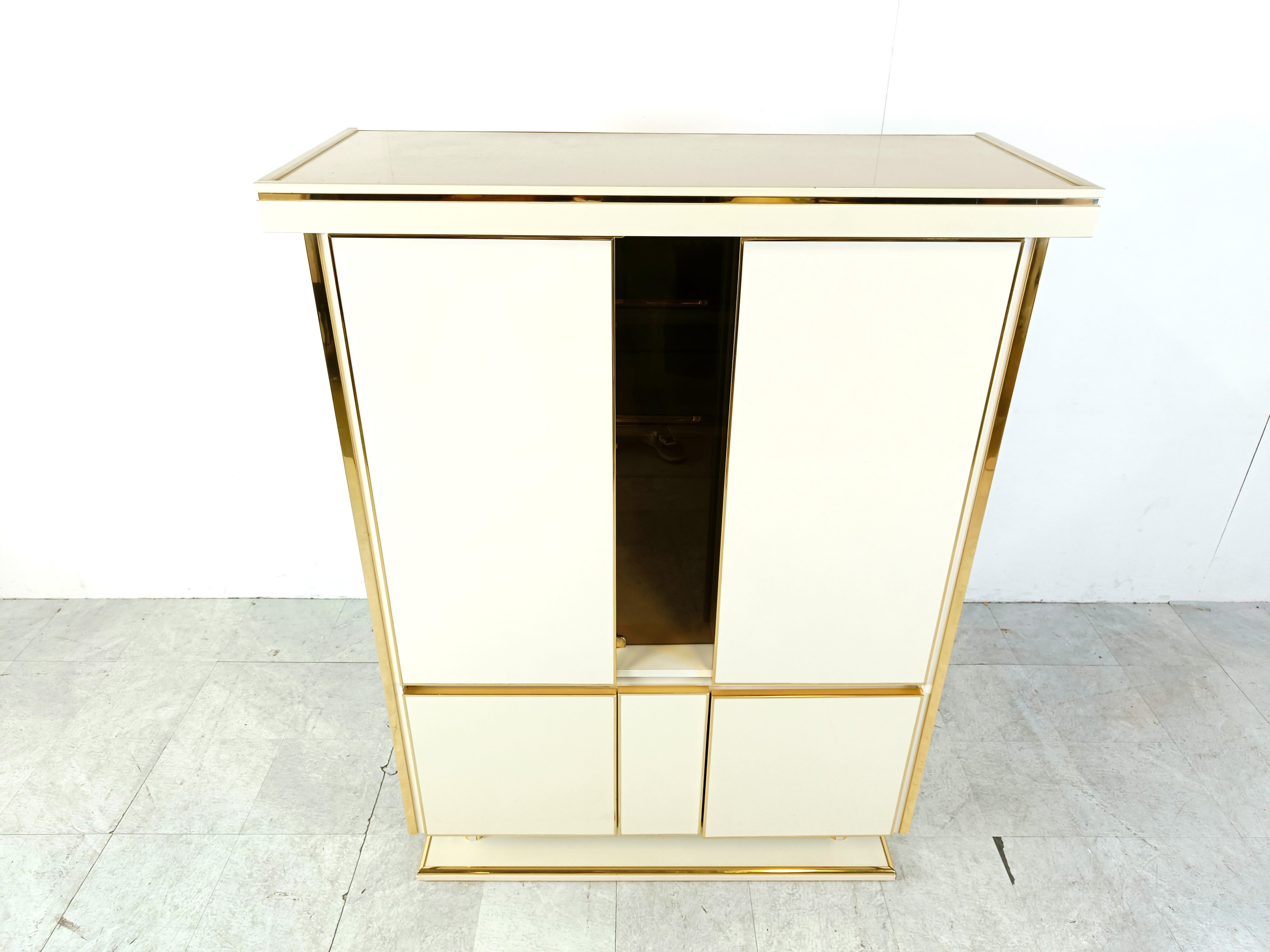 
Vintage seventies glam brass and white lacquer bar cabinet.

The bar is illuminated and offers plenty of storage space.

Glass and white wooden shelves inside.

1970s - France

Good overall condition, working light.

Dimensions:
Lenght: