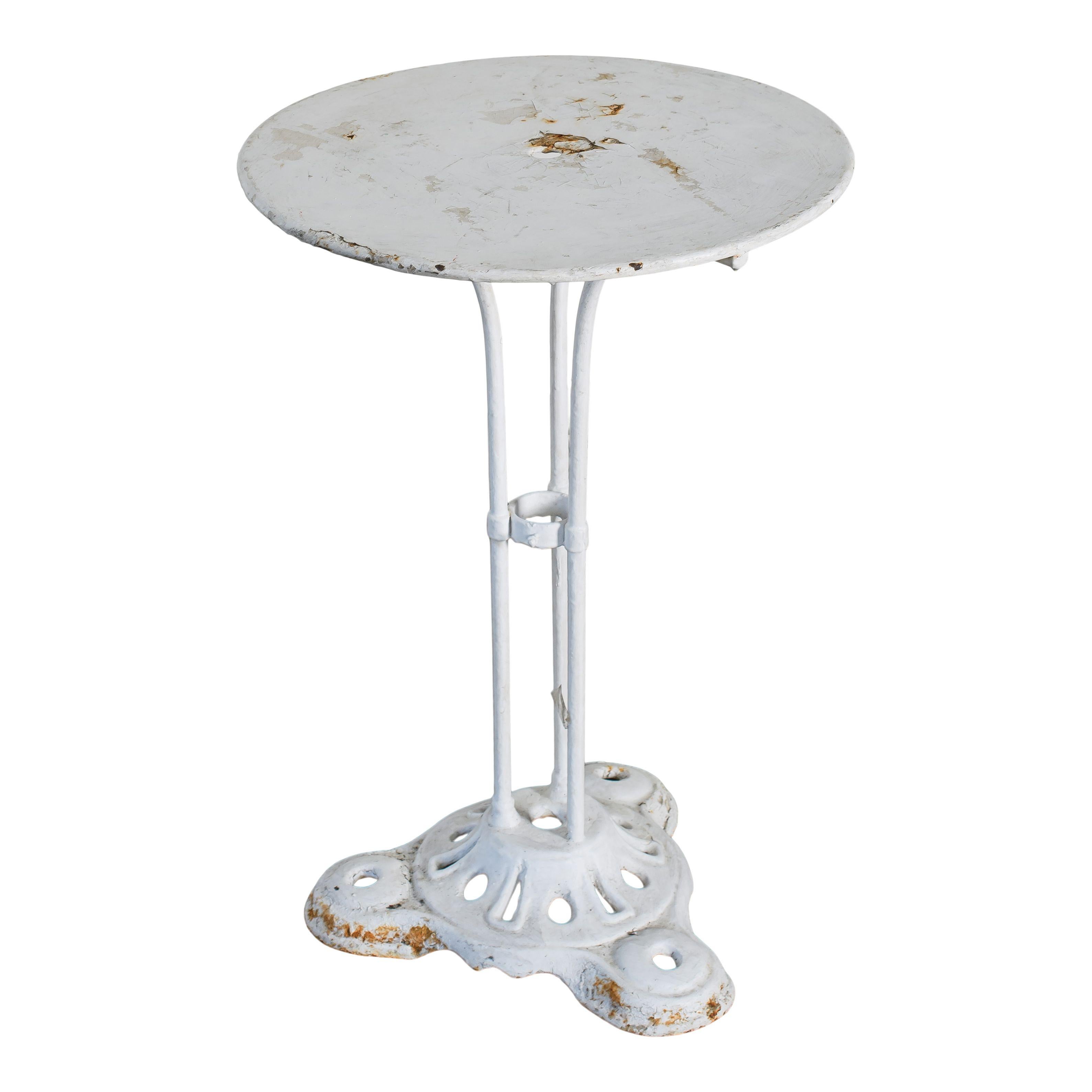 Une table de bistrot française vintage en métal et peinte en blanc. La peinture est écaillée et rayée à certains endroits, ce qui confère à cette pièce un joli charme vintage et une belle patine. Il y a trois pieds qui se rejoignent à la base, avec