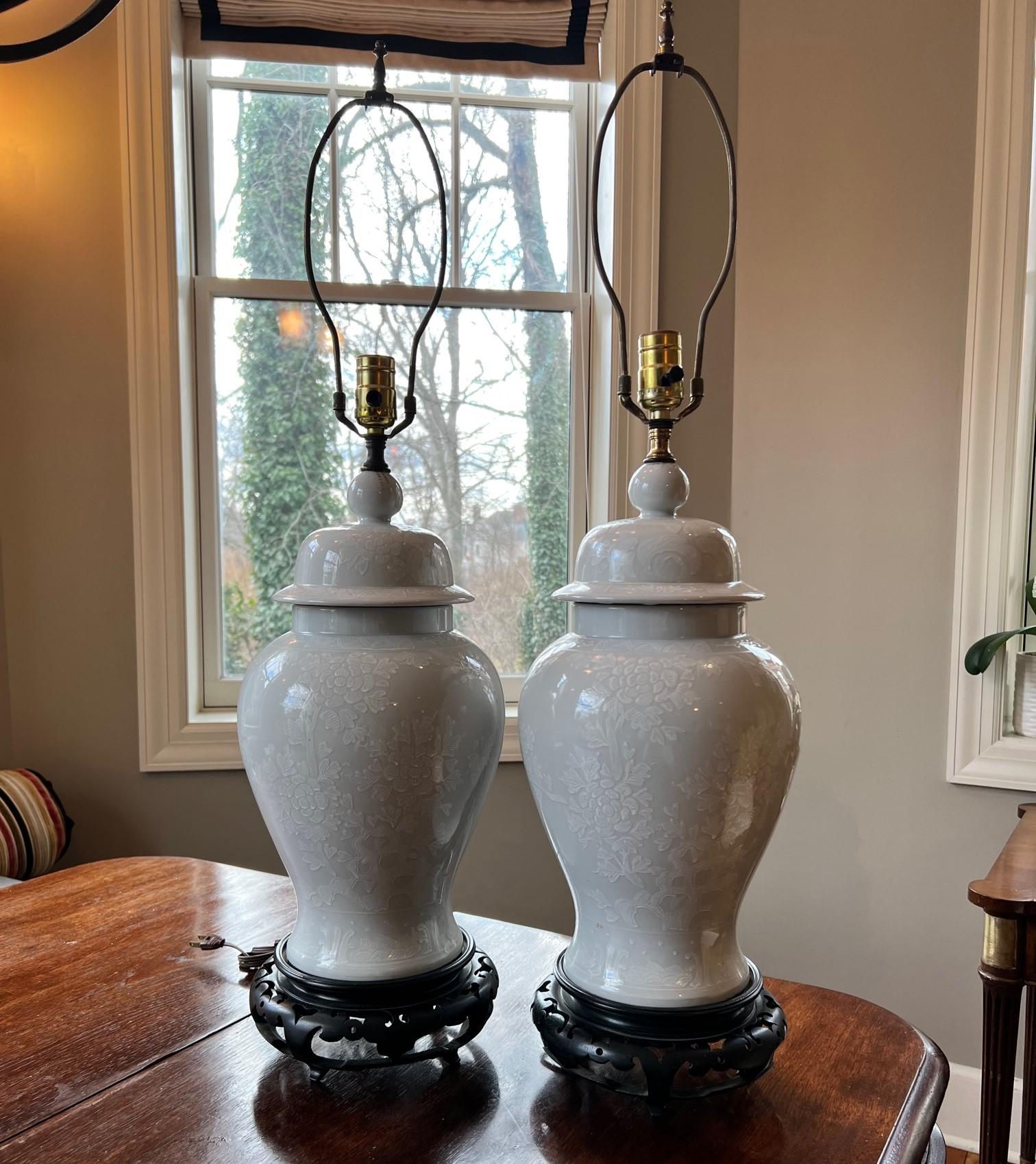 20th c., classic white porcelain ginger jars with white floral decoration, mounted as lamps, on pierced hardwood stands, unmarked. The scale of these lamps is impressive without being overscaled. They are not being sold with shades as the choice of