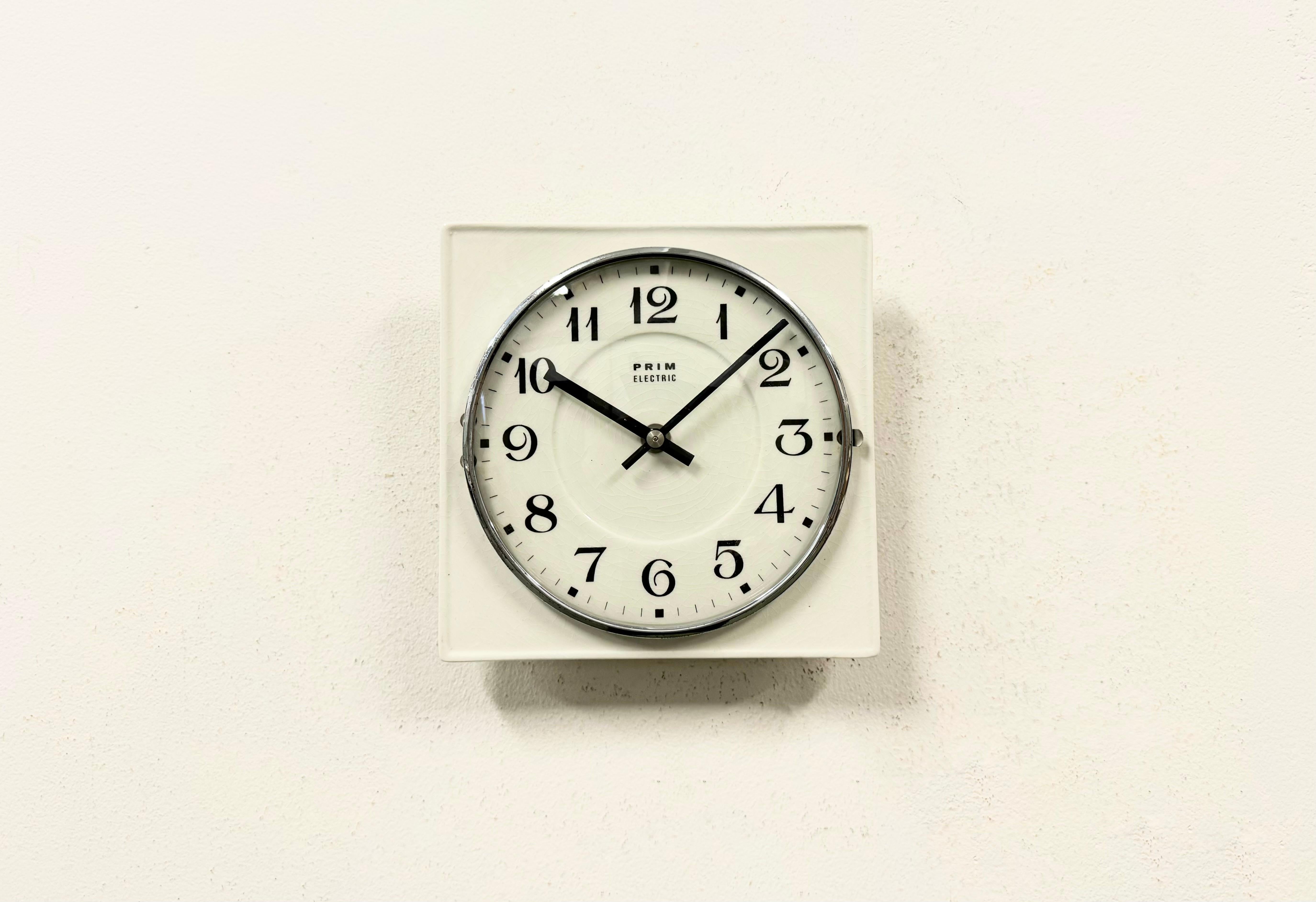 Vintage square wall clock was made by Prim in former Czechoslovakia during the 1970s .. It features a white porcelain body  and a convex clear glass cover with brass ring. The clockwork works perfectly and requires one AA battery.
The clock