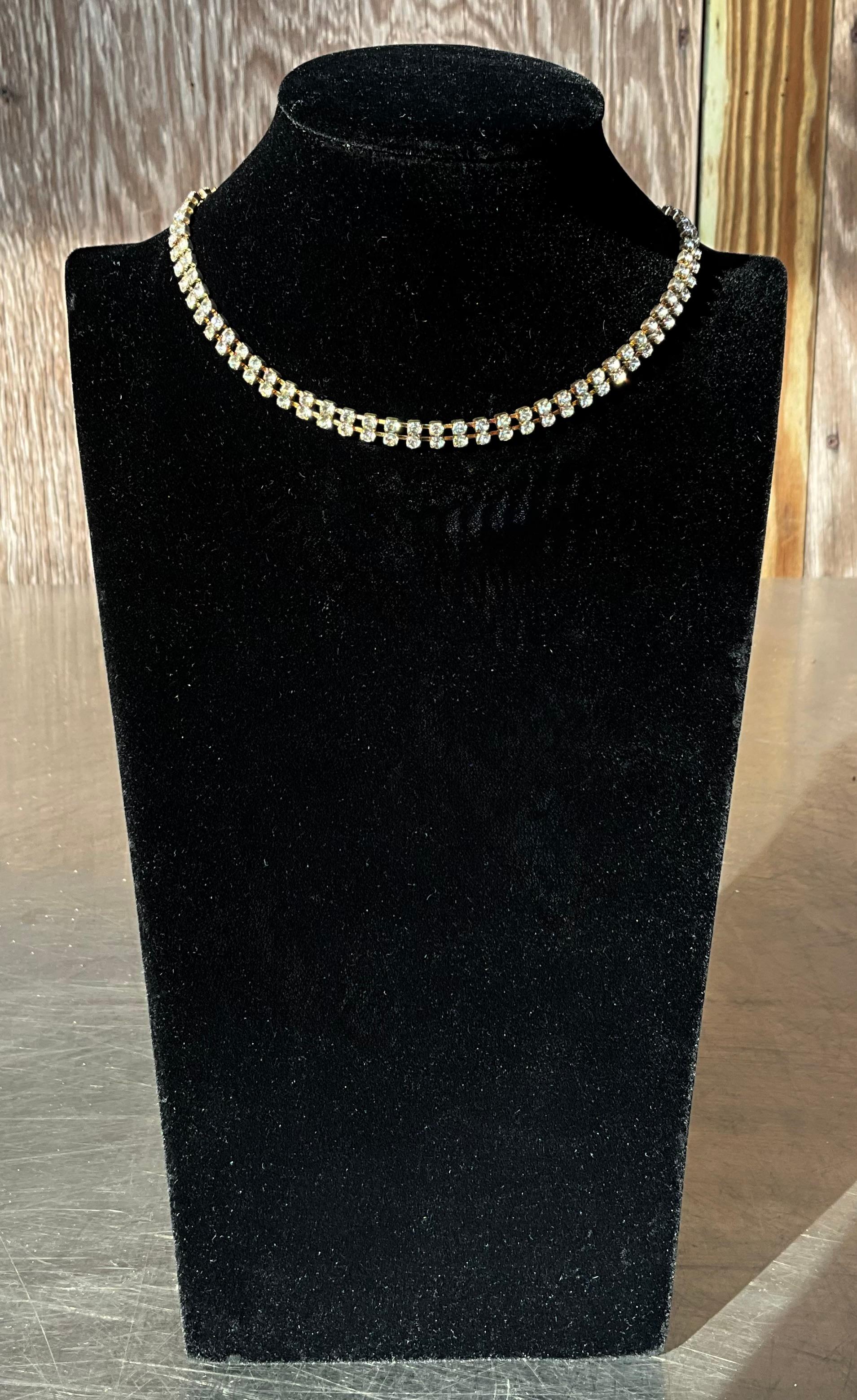 Questa collana vintage con strass bianchi è caratterizzata da un design straordinario con una serie di strass bianchi scintillanti incastonati in un girocollo aderente. Gli strass, che imitano la brillantezza dei diamanti, sono spesso incastonati in
