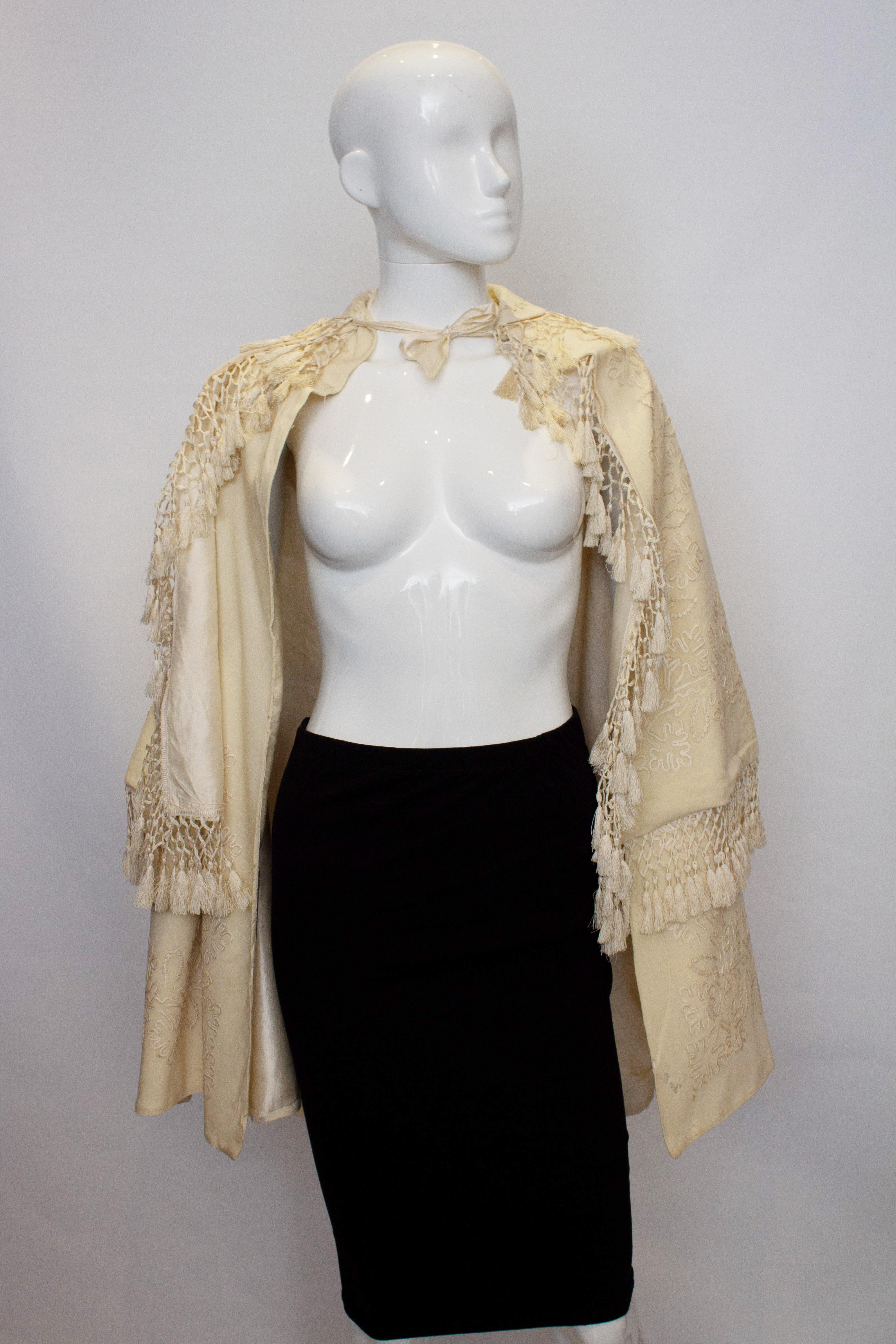 Ein wunderschöner weißer Wollumhang im Vintage-Stil mit Stickereien und Fransendetails. Die Jacke hat ein Band zum Binden im Nacken, und sowohl der Ober- als auch der Unterumhang sind bestickt.
Maße von Schulter zu Schulter 17'' Länge 37''