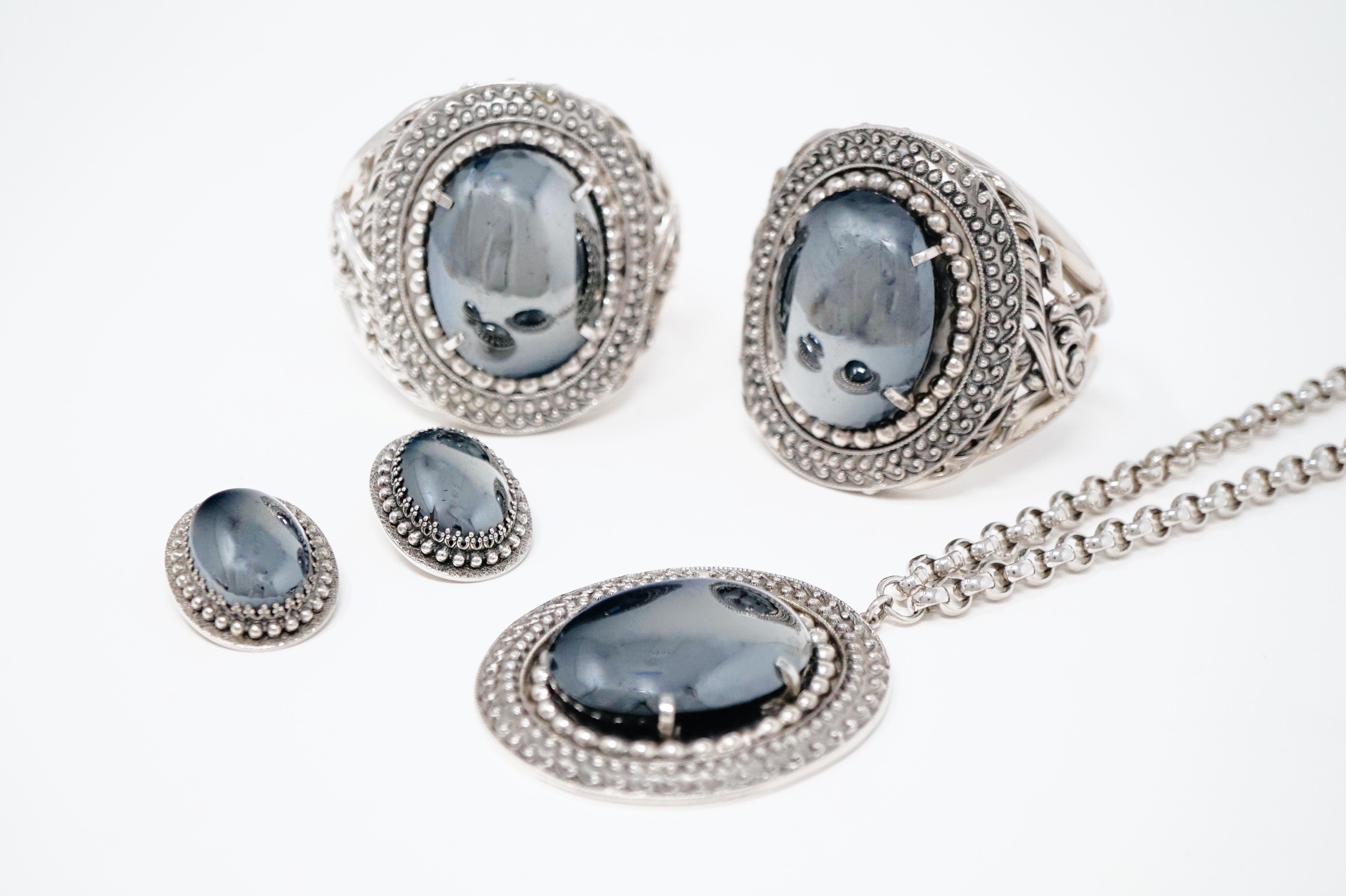 - Parure includes two hinged clamper cuff bracelets, pendant necklace and clip on earrings
- Silver tone
- Faux hematite
- Clamper bracelets measures 2.5