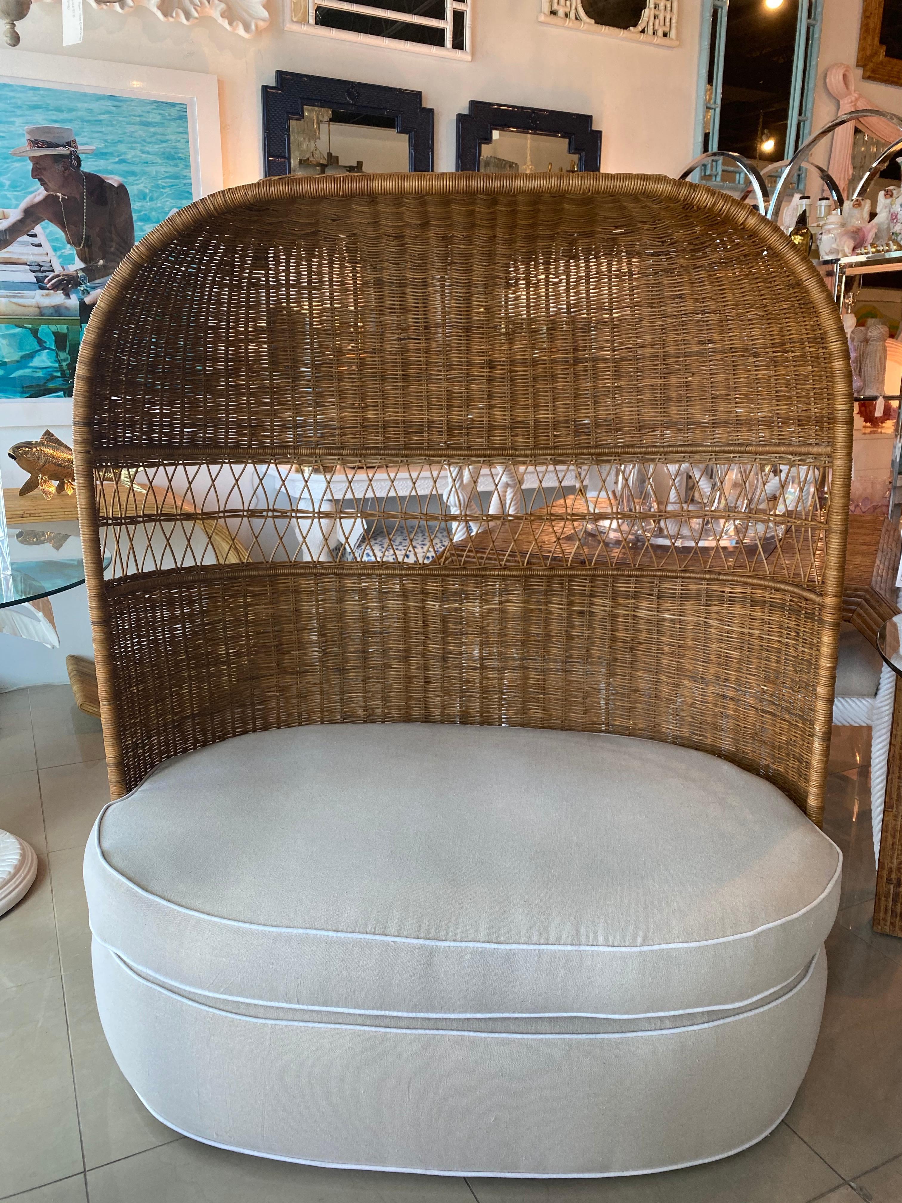 Lovely vintage wicker and rattan hooded settee loveseat chair. Newly upholstered in a Sunbrella cream fabric with white trim. Wicker is intact with no missing pieces. 
Cushion depth is 32.