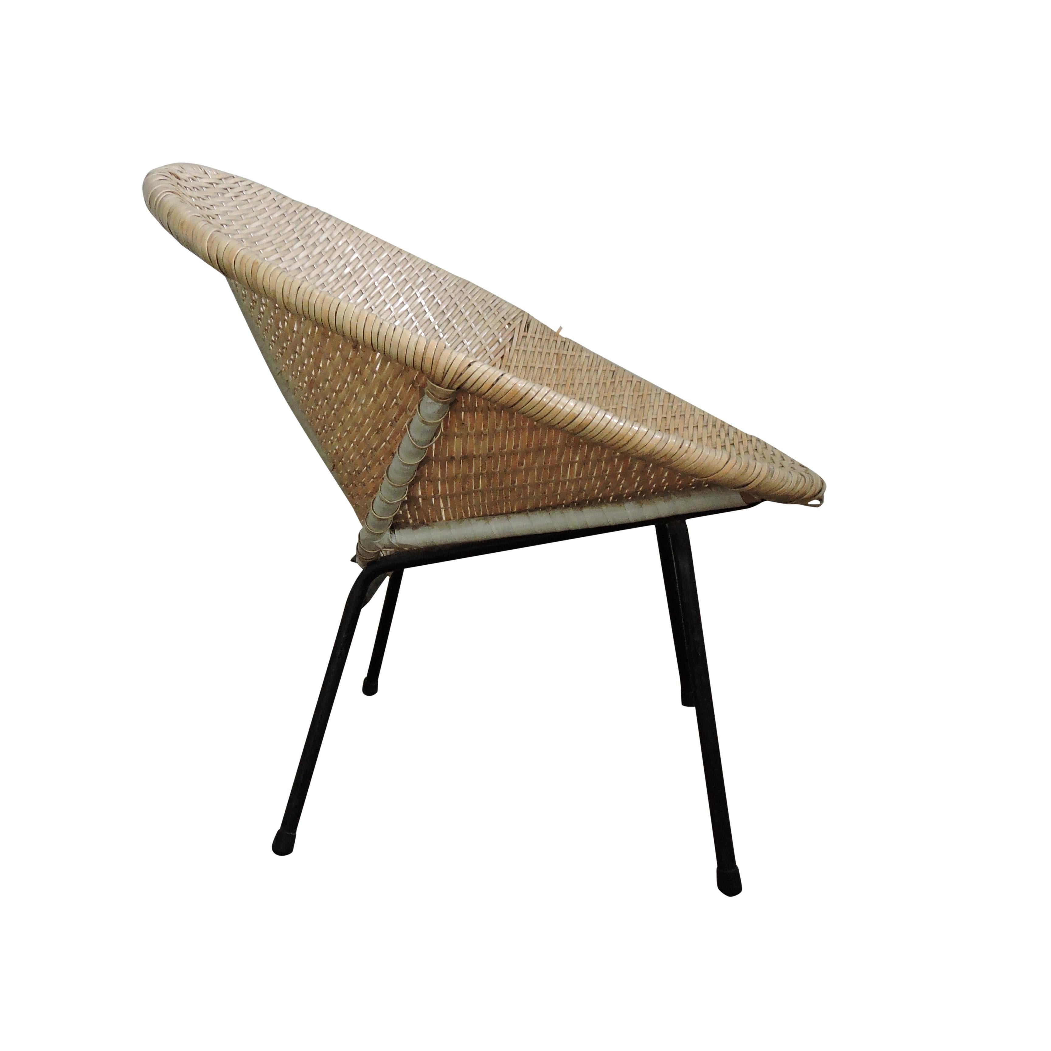A vintage wicker bucket chair sitting on four black metal legs.