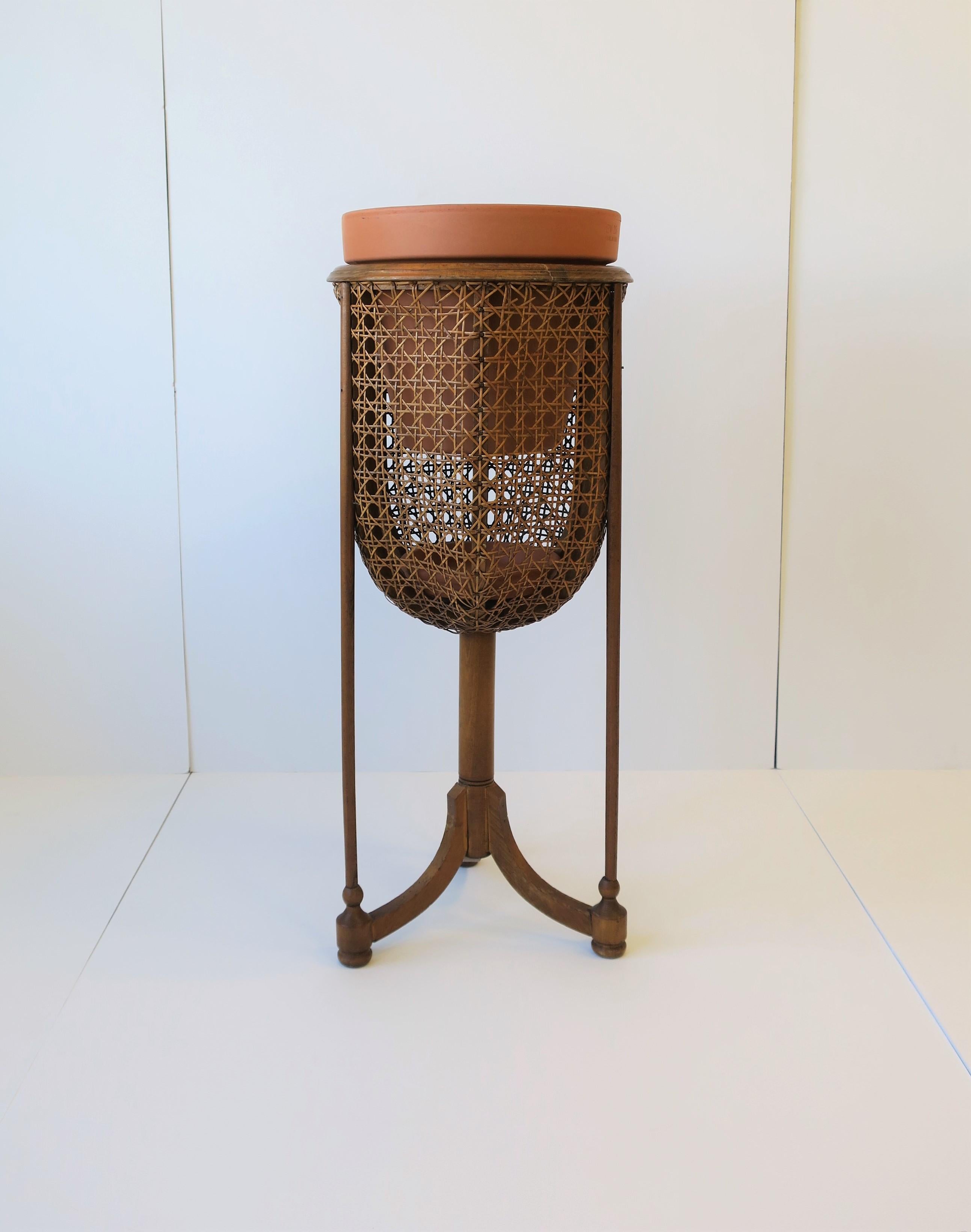 A beautiful vintage wicker cane plant stand with tri-pod base/legs, circa 1960s-1970s. Plant Stand has a beautiful round basket and relatively large caning and a bentwood top or rim. Piece takes a 10