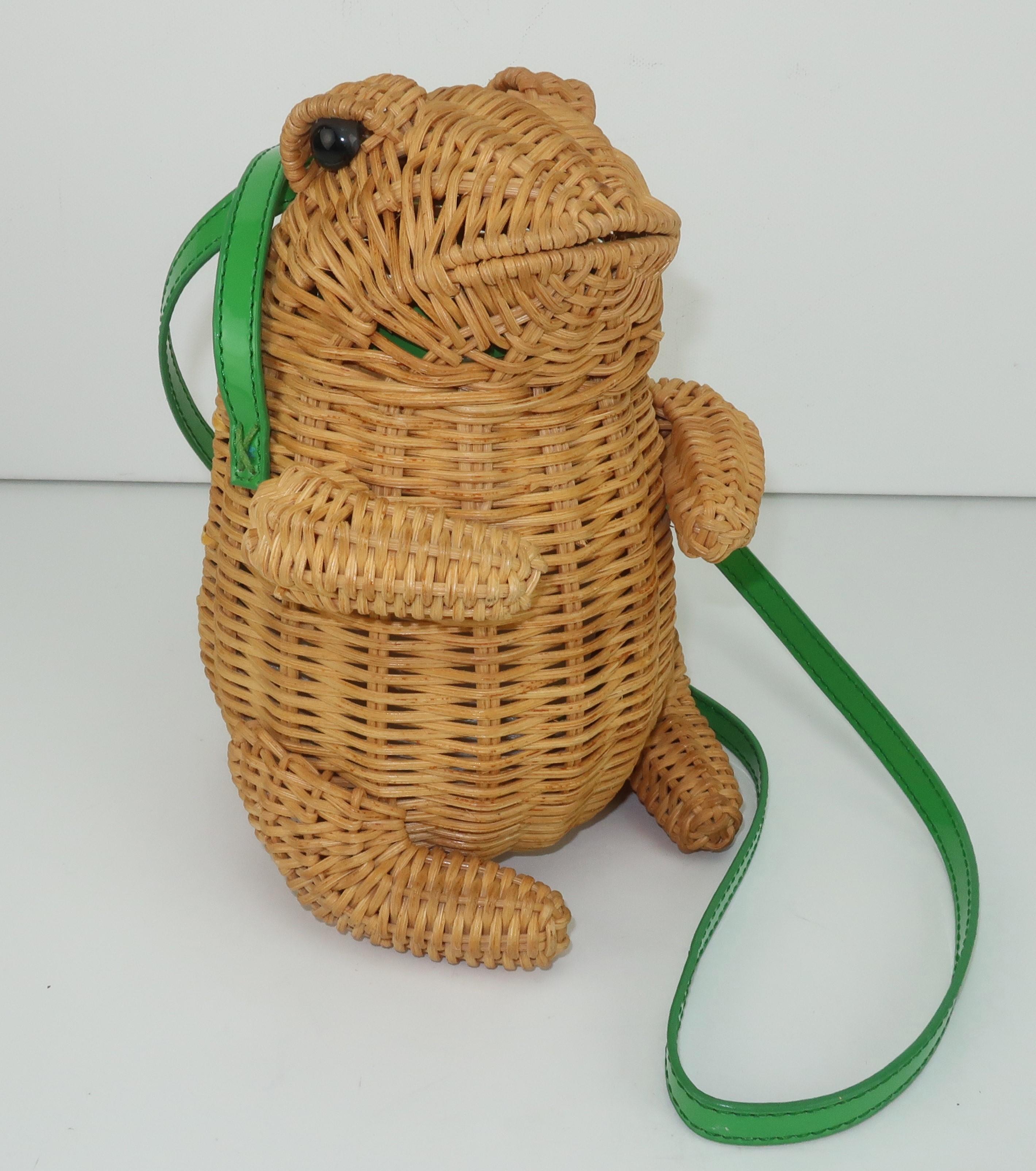 Natural wicker handbag in the shape of an adorable frog with green patent shoulder strap, glass eyes and a discreet trap door opening.  The interior is lined in green patent and the trap door closes with a metal button and green elastic.  He will