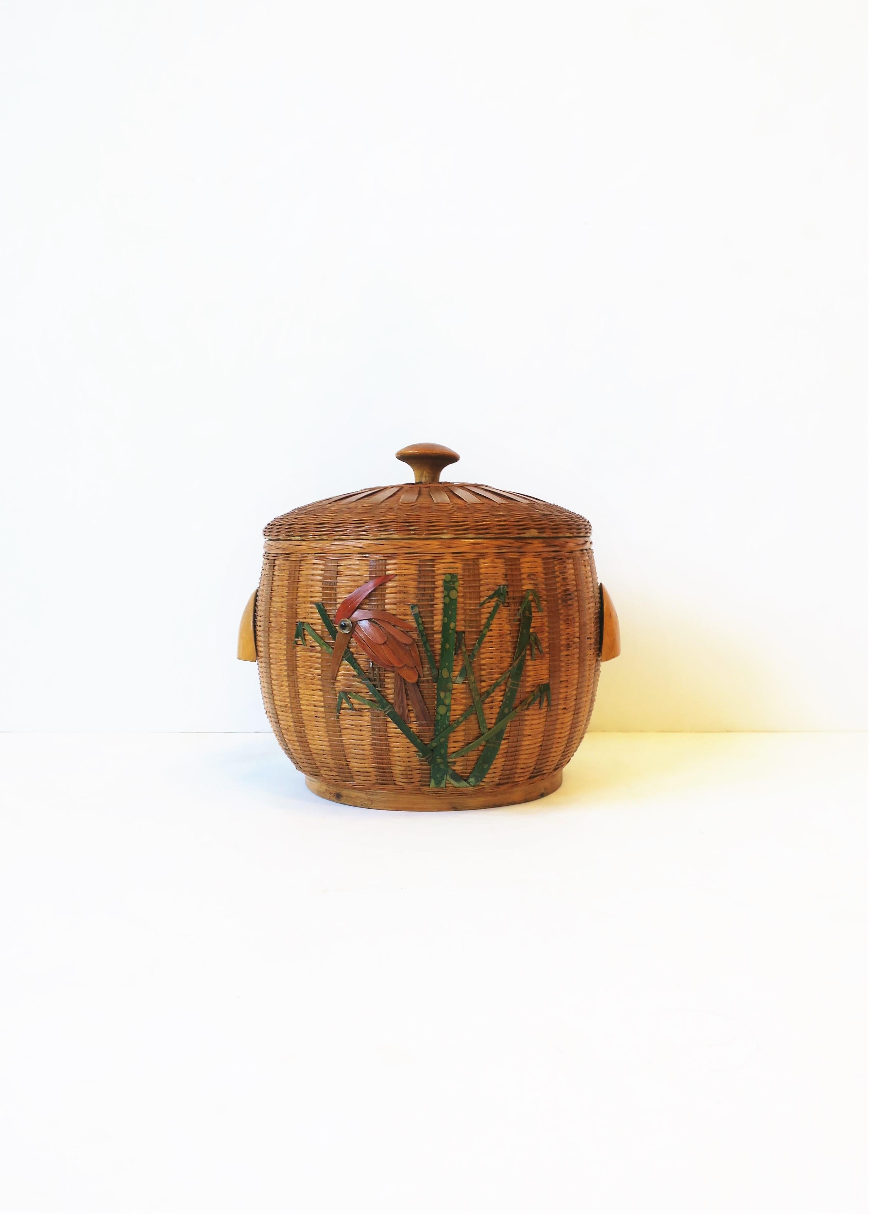 A beautiful vintage wicker ice bucket with enamel metal interior pot and lid. Beautiful wicker design embracing enamel pot and lid, and a bird on bamboo branch design on front. Small wood handles on sides. Round wood knob on lid. Piece is early to