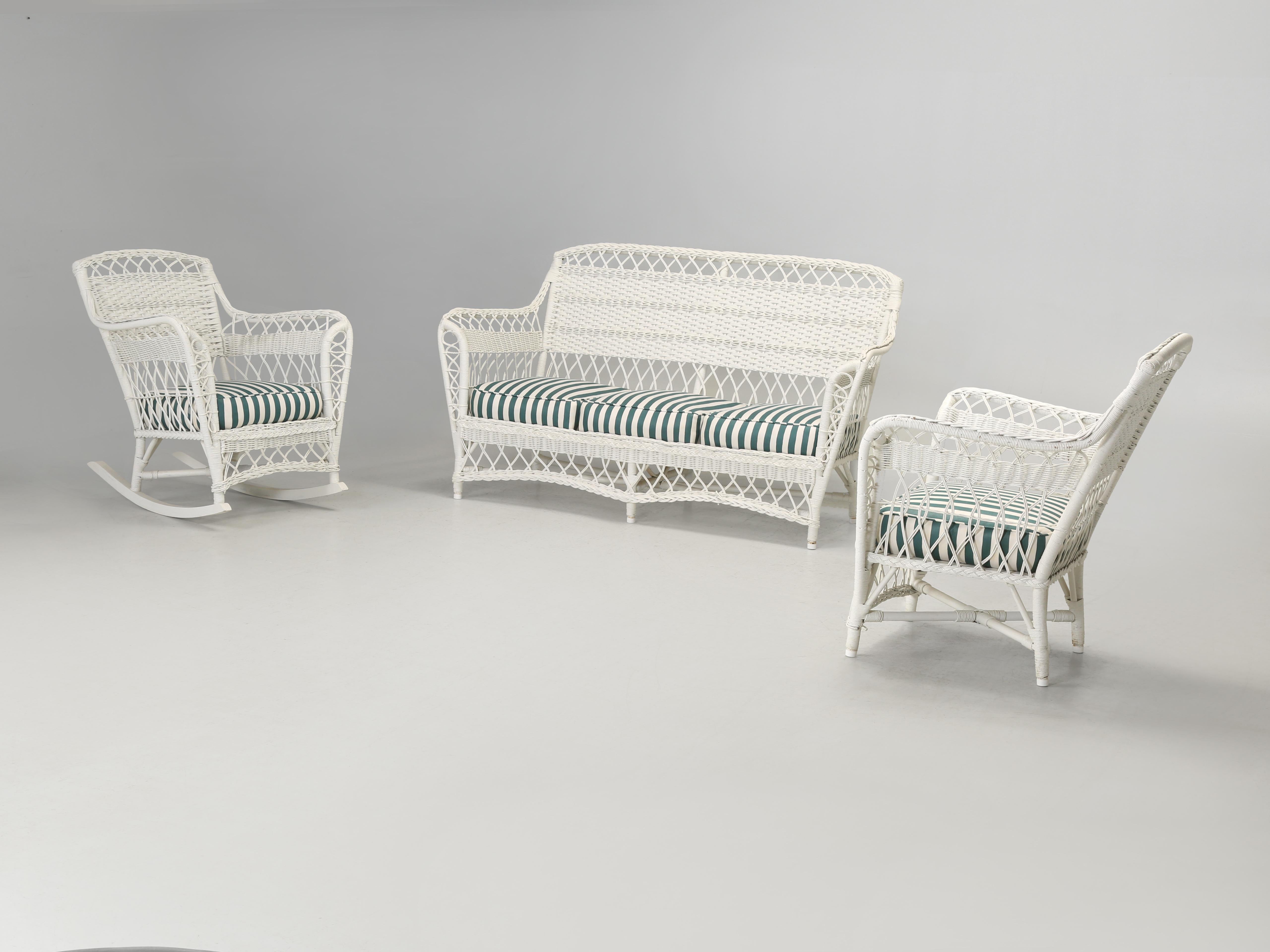 Conjunto vintage de mimbre que incluye un sofá de mimbre, una silla de mimbre y una mecedora de mimbre, todos ellos utilizados en una terraza interior y no expuestos a la intemperie. Hay una mancha en un cojín del asiento, pero el estado del mimbre