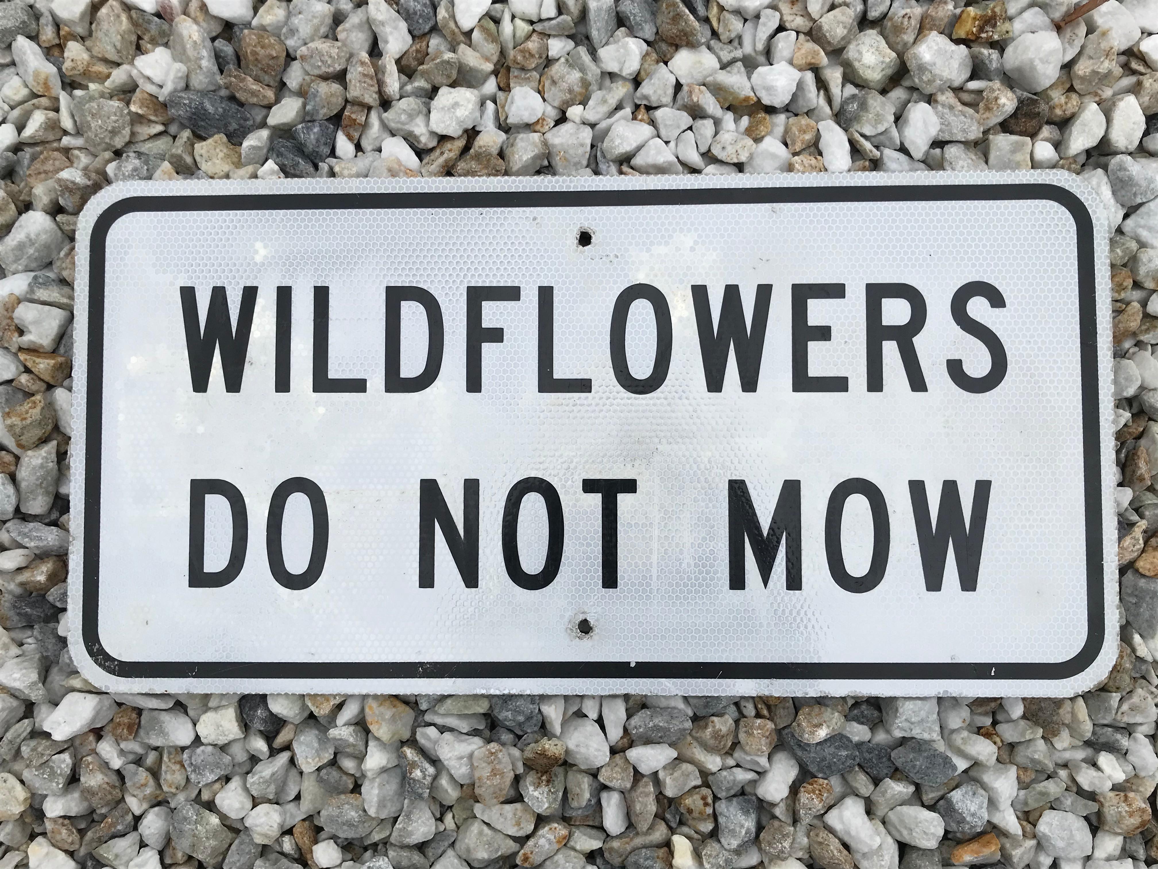 Great vintage highway sign that reads Wildflowers Do Not Mow. Reflective gray sign with black lettering and trim. Fun wall art and cool piece of transportation history.