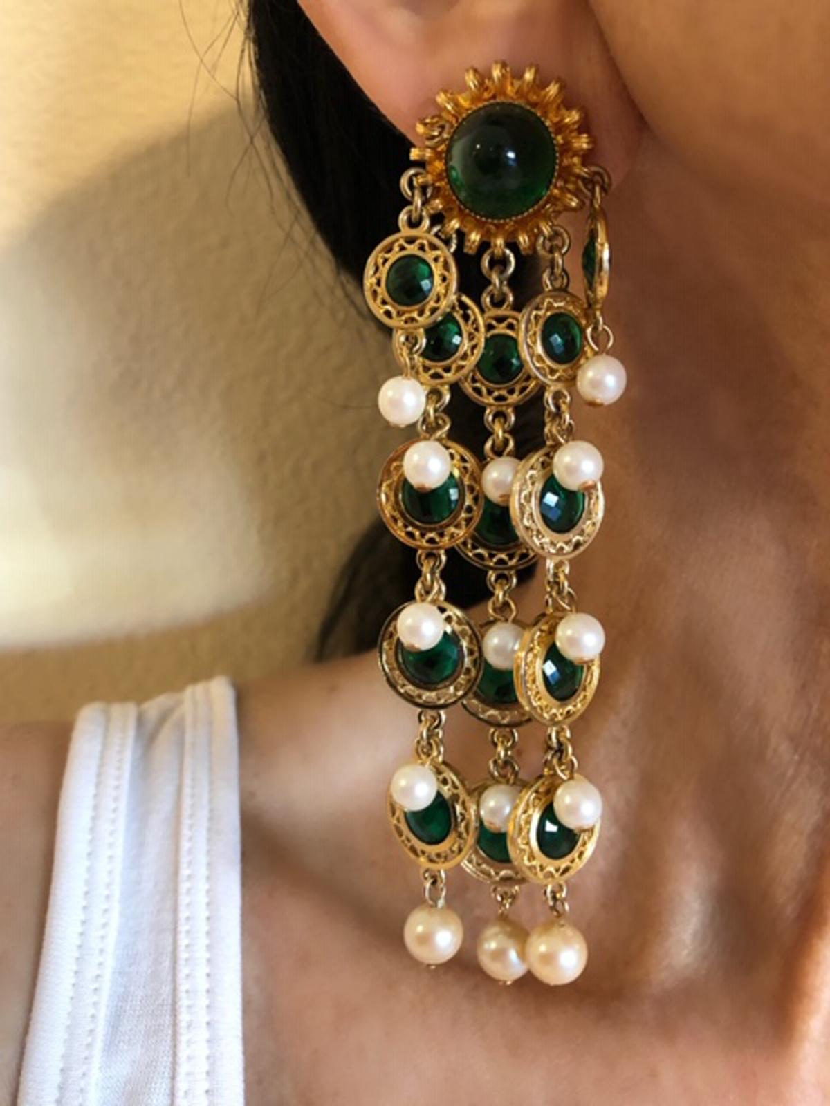 Beautiful pair of faux emerald and pearl earrings by William de Lillo. The statement clip-on earrings are comprised of highly detailed gold-tone circular beads which are accented in the center by faux glass emeralds - the chains and segments are