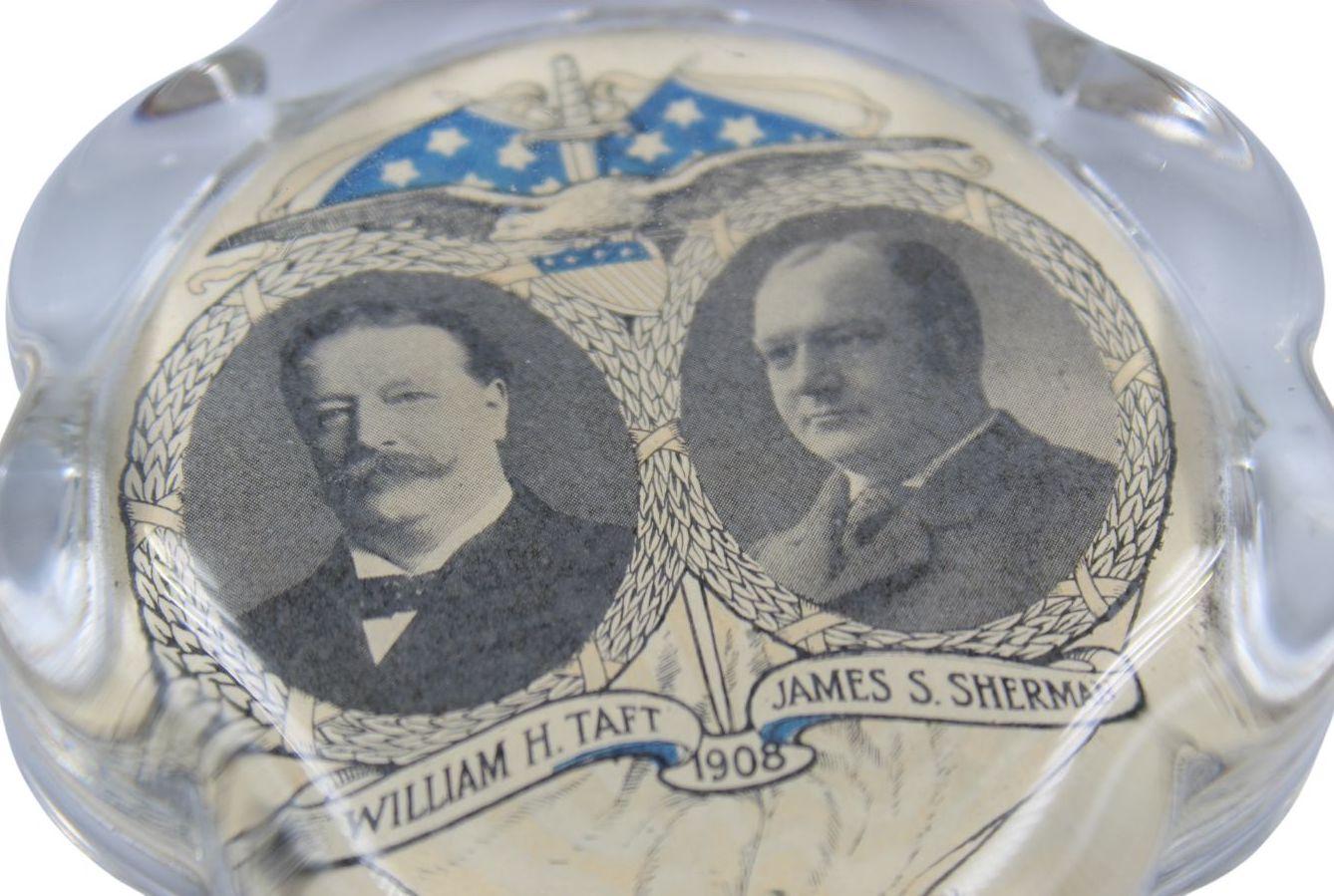 Presented is a vintage William H. Taft and James S. Sherman presidential campaign glass paperweight from 1908. The clear glass paperweight has a flower form, with a printed and enameled political jugate at the bottom. Two oval black and white