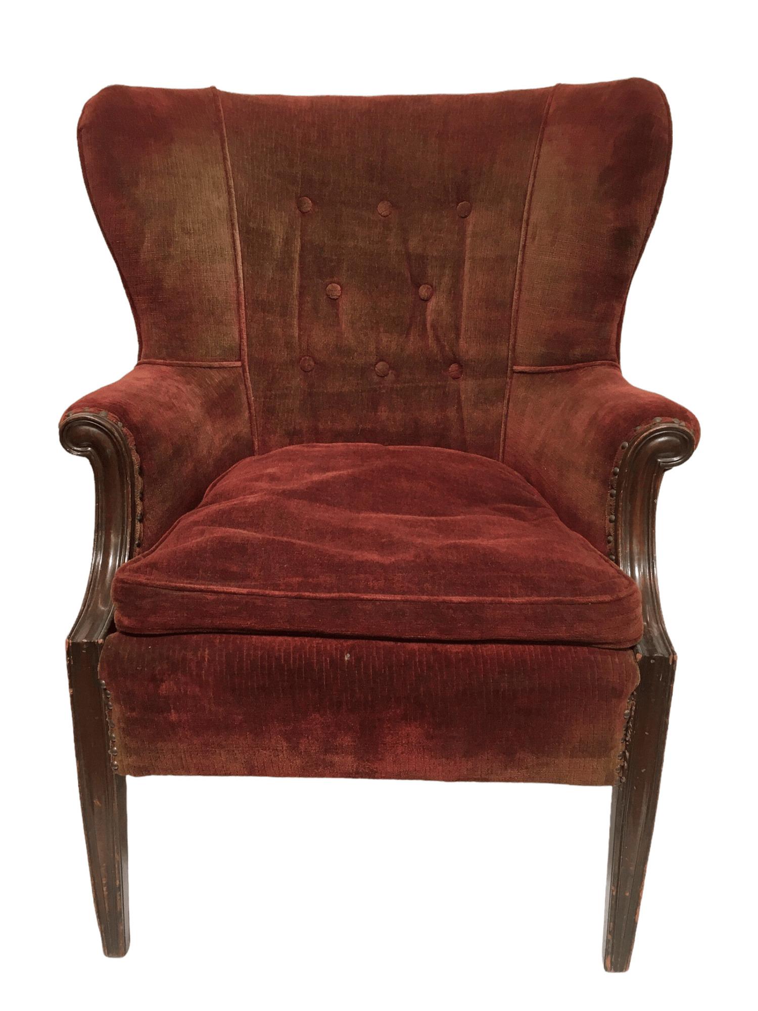 Vintage Wingback armchair upholstered in a light red fabric that fades in areas almost to brown. This armchair features mahogany wood legs, armrests with a subtle scrolling detail, and a button-tufted padded backrest.
 
It has signs of age that give