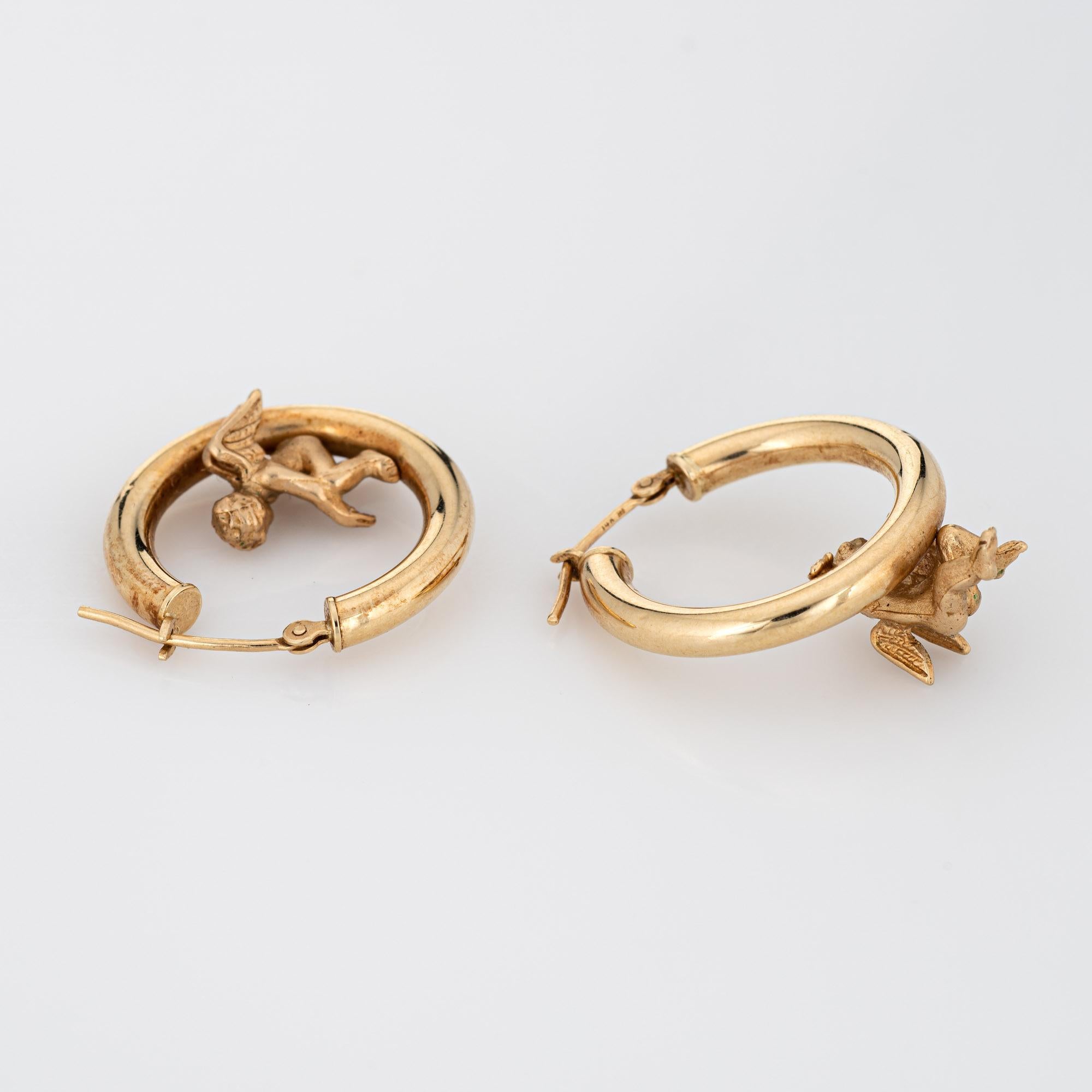 Finely detailed pair of vintage winged angel hoop earrings crafted in 14k yellow gold (circa 1990s). 

The charming earrings highlight two winged angels, one sitting within the hoop with the other climbing up to the hoop. The hollow earrings offer a
