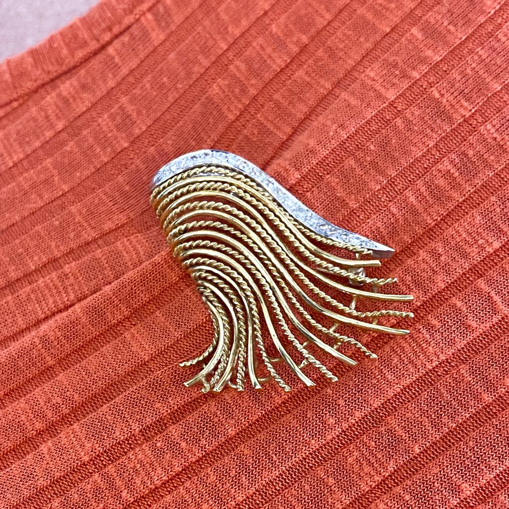 Vintage beauty shines bright in this classy 1940s brooch made with sleek and sweeping curves of 18 karat gold wirework and a ribbon of bright platinum set with old single cut diamonds. This takes you back to a time when quality craftsmanship was