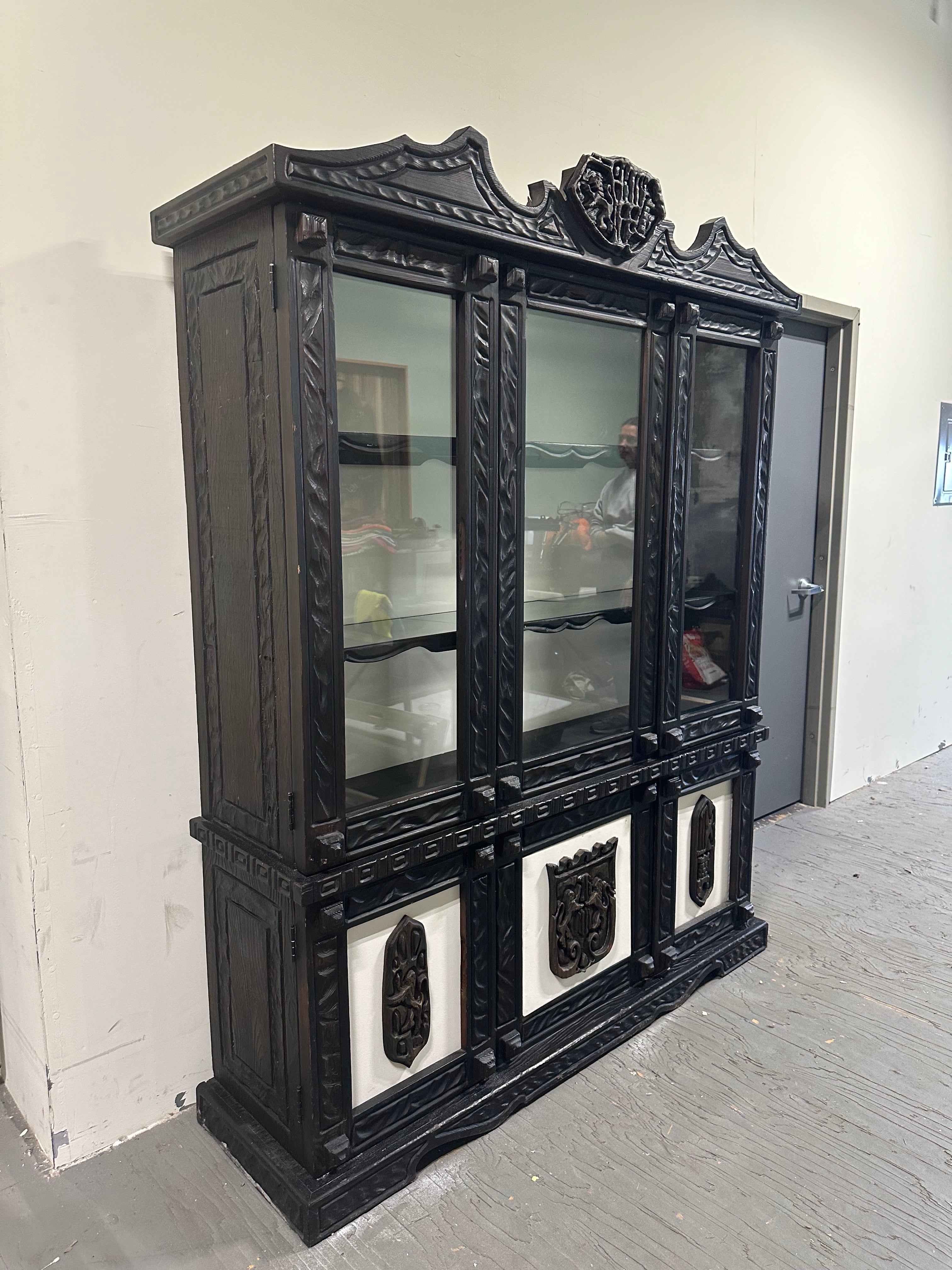 Unique and rare William Westenhaver styled cabinet. Classic Witco TiKi style with a touch of Gothic elements. Lion Crested top and great carved elements  throughout. 3 glass shelves in upper lighted cabinet along with 2 drawers and shelves in lower