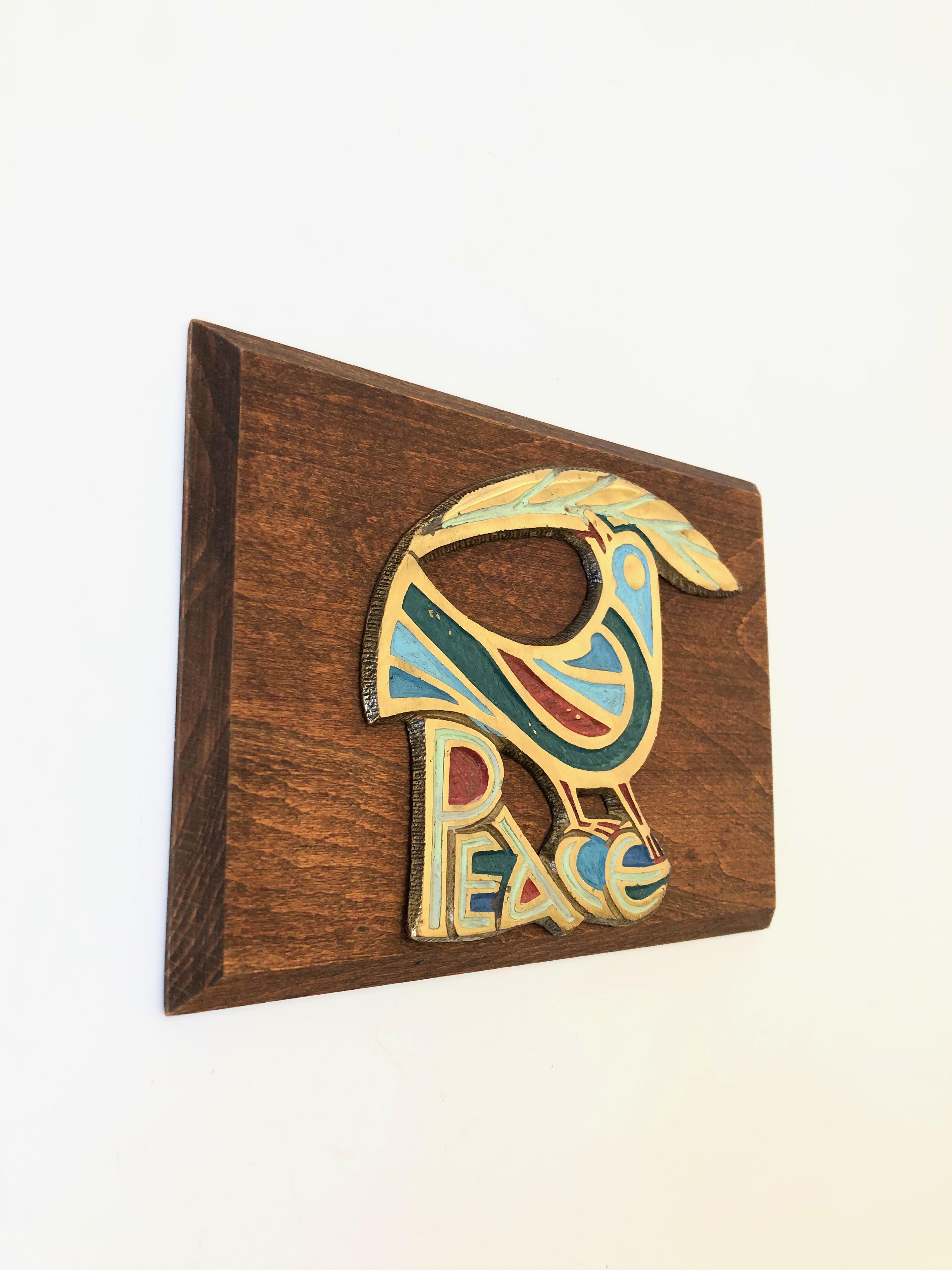 A vintage wood and brass wall plaque with the design of bird and the word 