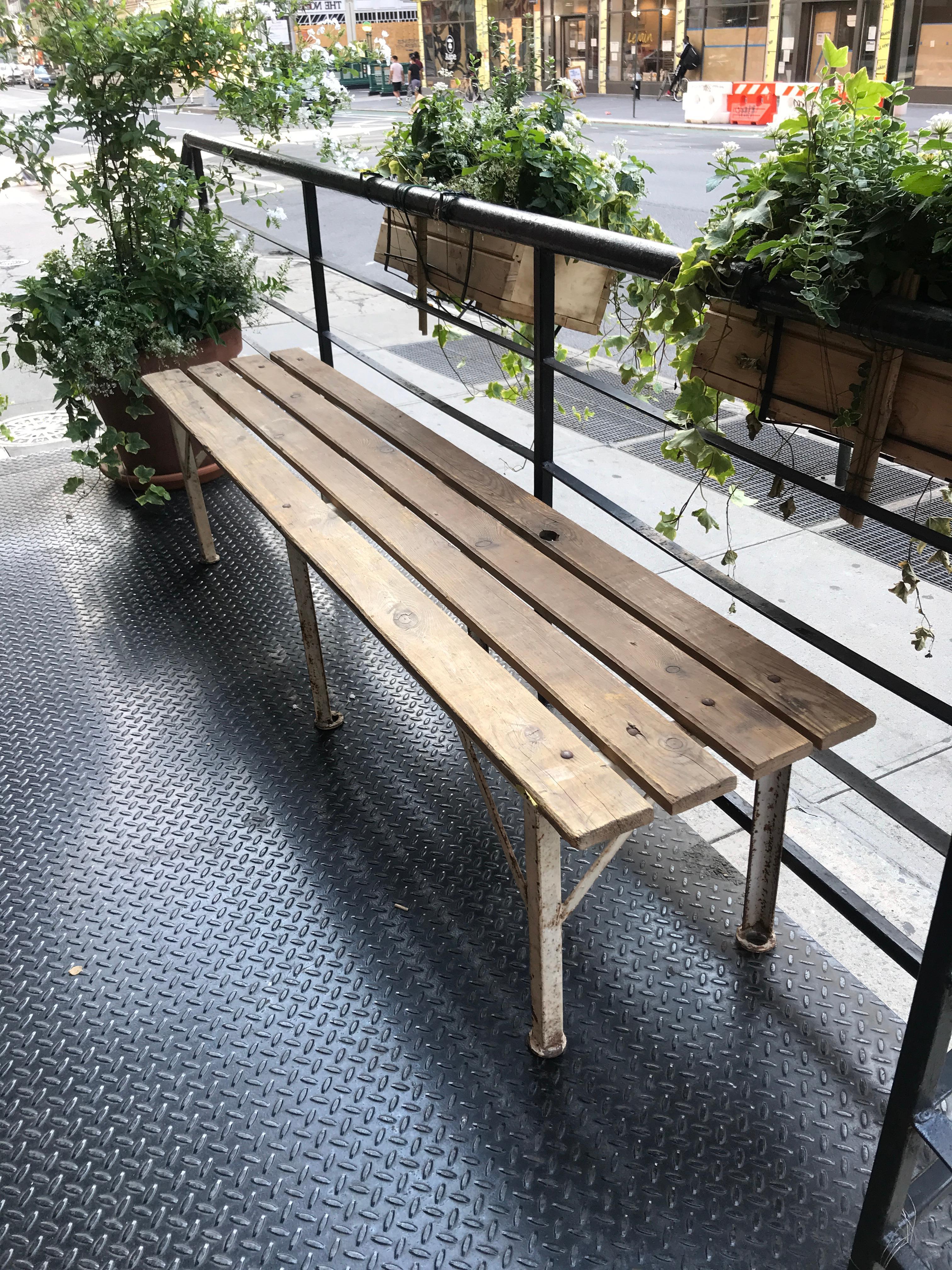 A rustic and weathered wooden plank bench with white painted metal legs. Perfectly sized for a long patio or entry hallway to seat after a long day.