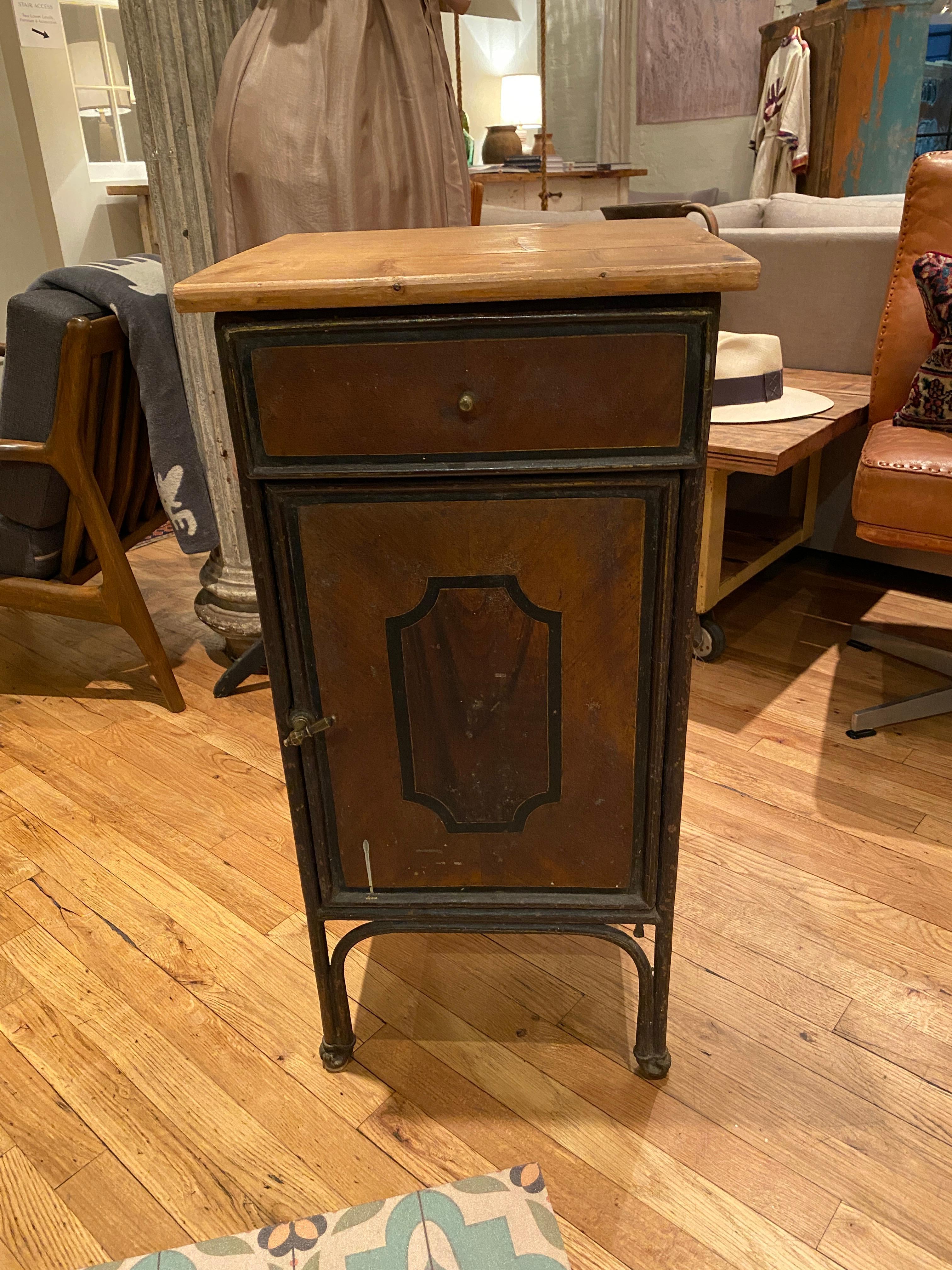 This beautifully aged vintage nightstand is a versatile piece that lives up to its industrial aesthetic; with a weighted metal body this piece is meant to last. Artistically painted wood facade to mimic rich mahogany. Can be used a nightstand, end