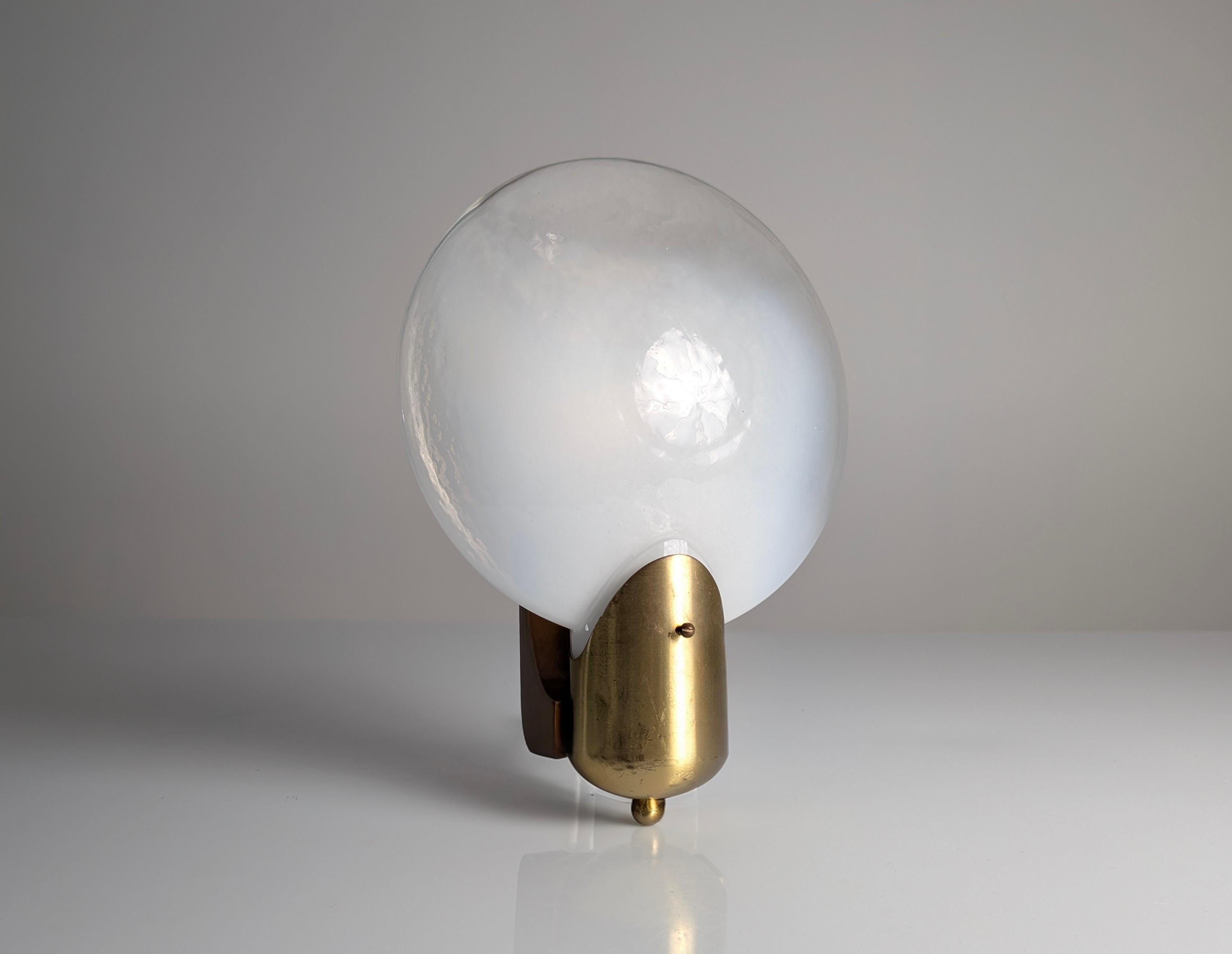 Applique italiana prodotta negli anni '70 con diffusore in vetro di forma ovale. Il vetro presenta una finitura bianca con un profilo superiore sfumato, che crea un effetto di luce soffusa. La struttura è composta da una base in ottone dorato che