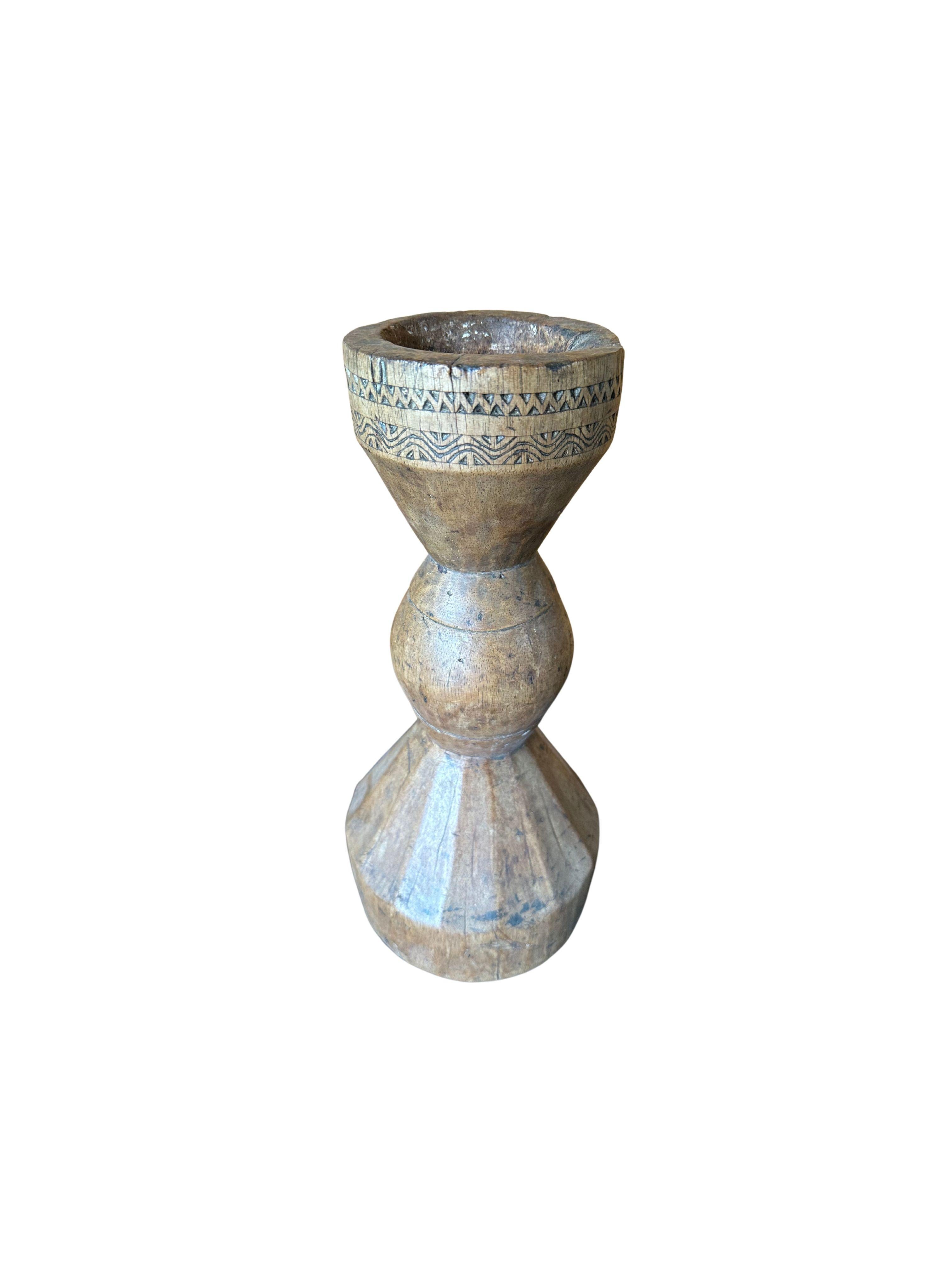 A vintage candle holder from the island of java. This candle holder features carved detailing around its shoulder. A wonderful sculptural object to bring warmth to any space. The age related fading of the wood, wood textures and shades add to its