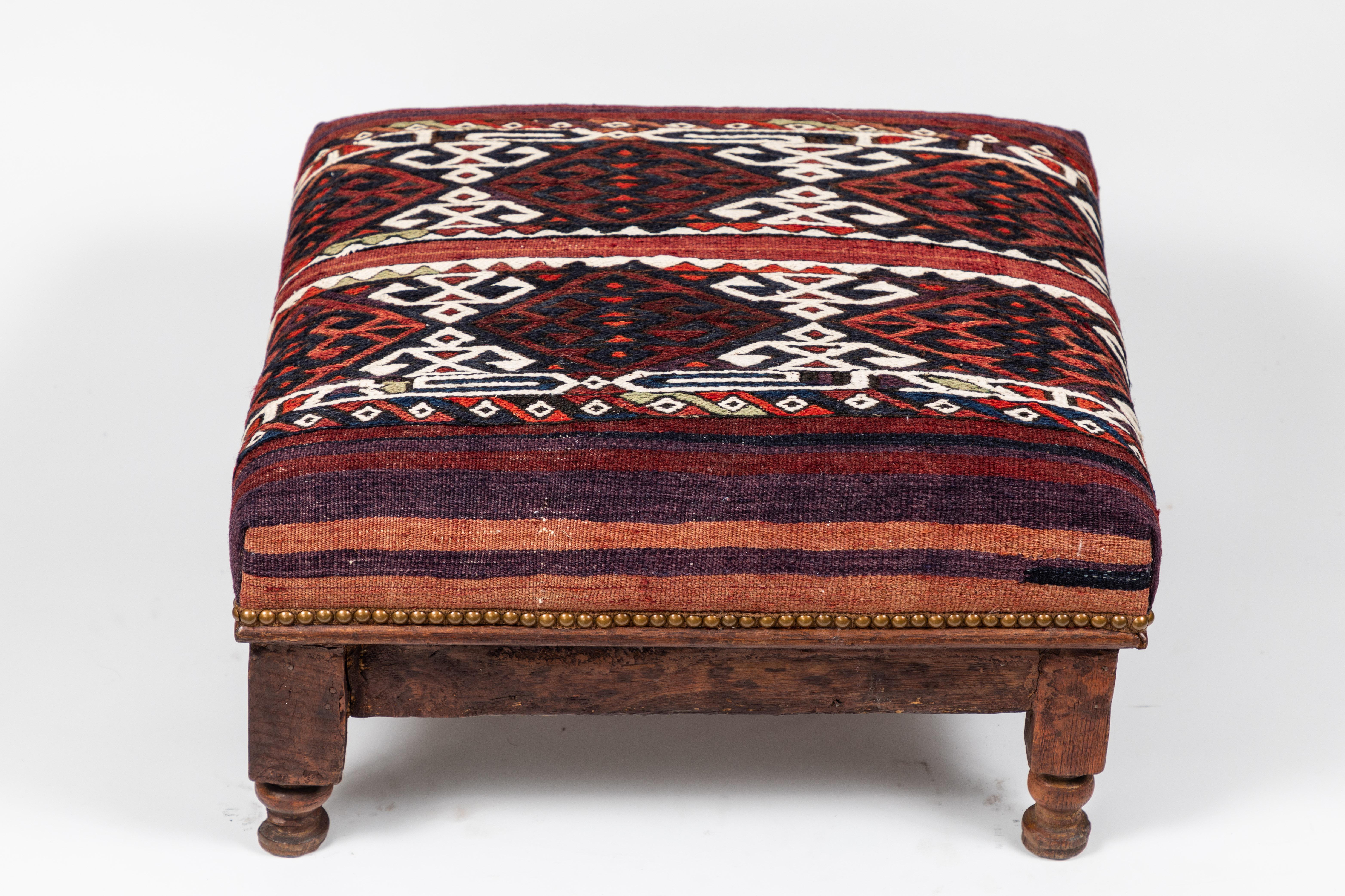 Fabulous squat vintage wood foot stool has been newly upholstered in a handsome vintage Turkish wool rug with dynamic pattern and a decorative nailhead trim detail.